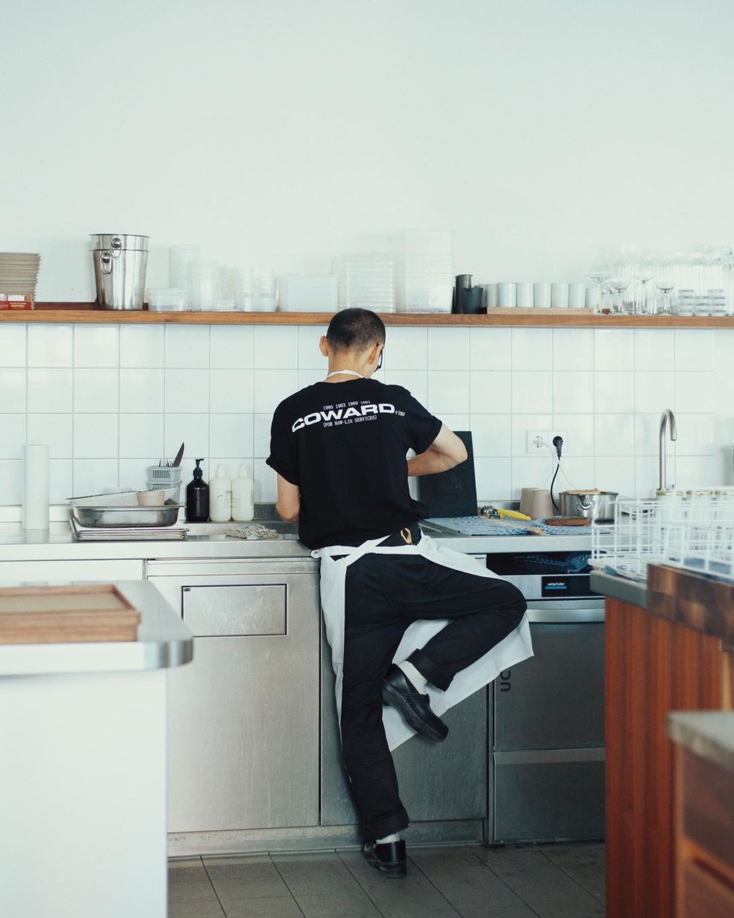 Julius in Berlin — In this kitchen detail from Julius Berlin, a figure in black Conward-branded sportswear sits at the counter, captured from behind.
