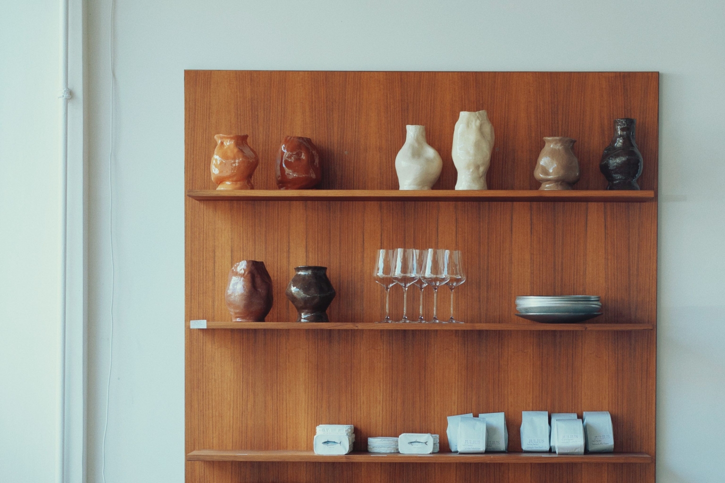 Julius in Berlin — A walnut wood shelving system displays a curated collection of ceramic vessels and glassware against a vertical wood-grain backdrop.