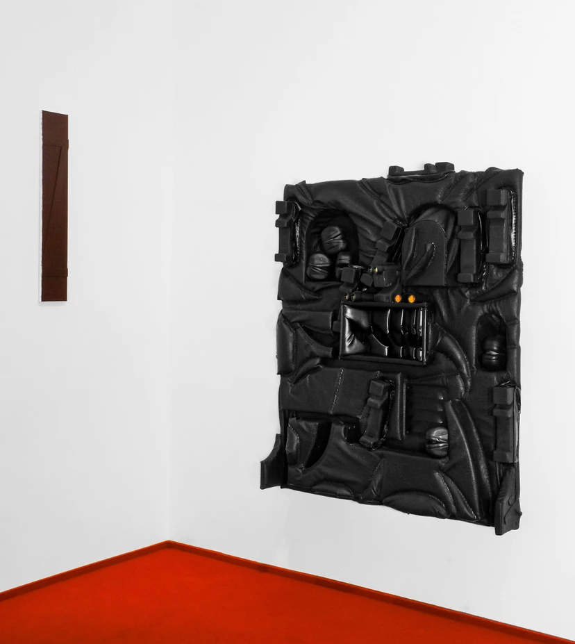 Productive Narcissism at 032c Gallery in Berlin — A wall-mounted sculptural installation rendered in inflated black fabric and plastic forms, presenting an abstracted, mask-like visage with two illuminated...