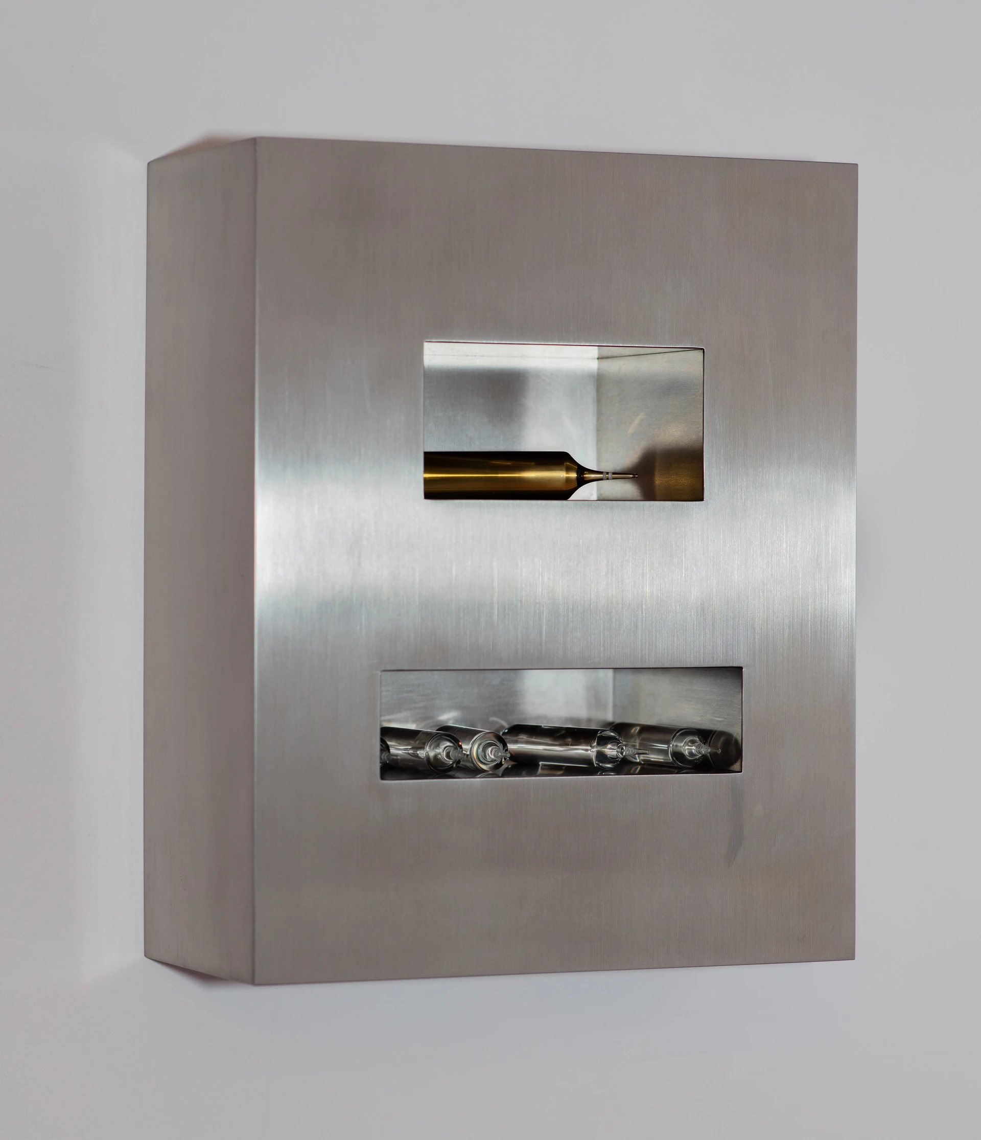 Productive Narcissism at 032c Gallery in Berlin — A brushed stainless steel display cabinet with two horizontal rectangular apertures reveals sculptural contents within.