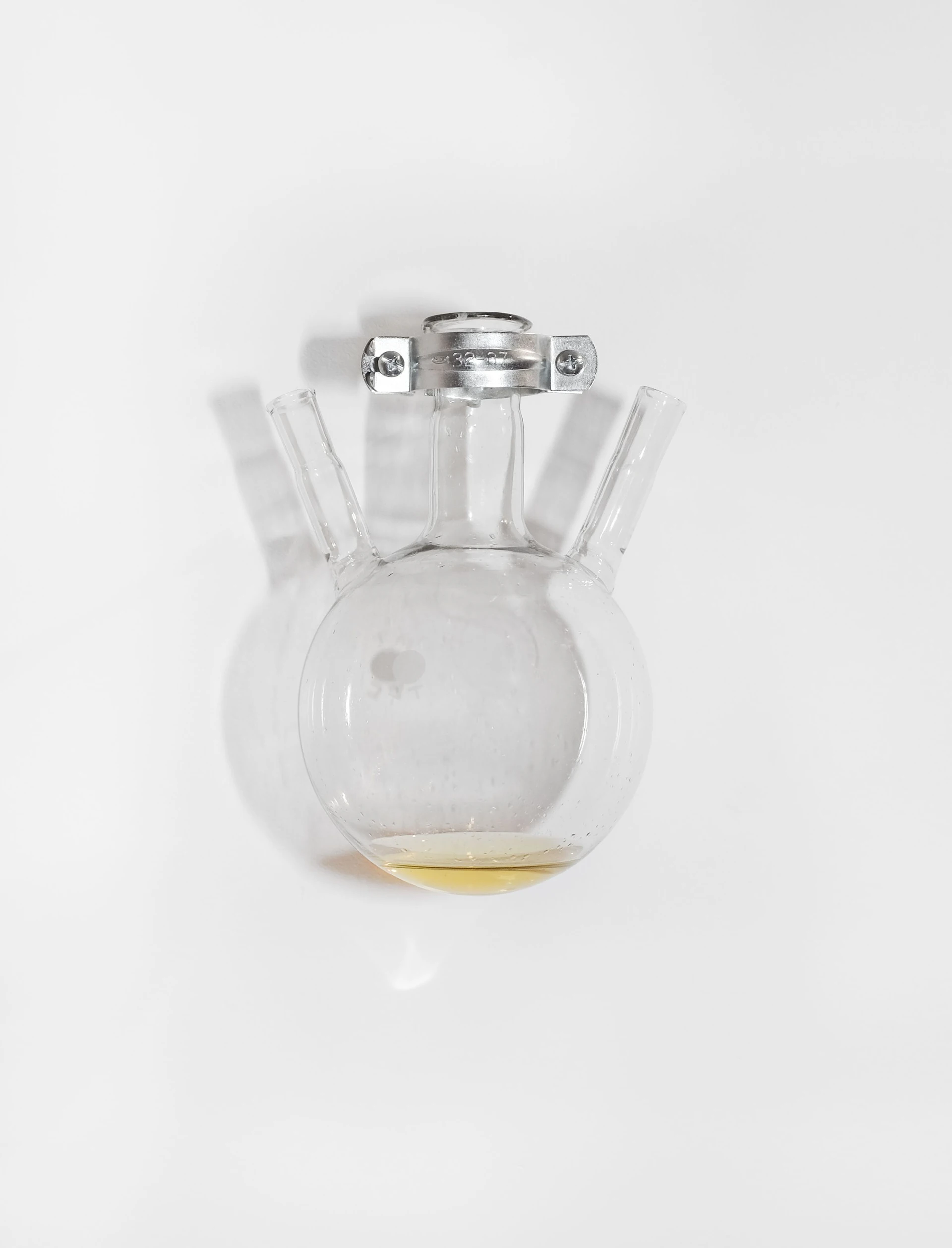 Productive Narcissism at 032c Gallery in Berlin — A clear glass vessel with a spherical bulbous body contains pale yellow liquid at its base.