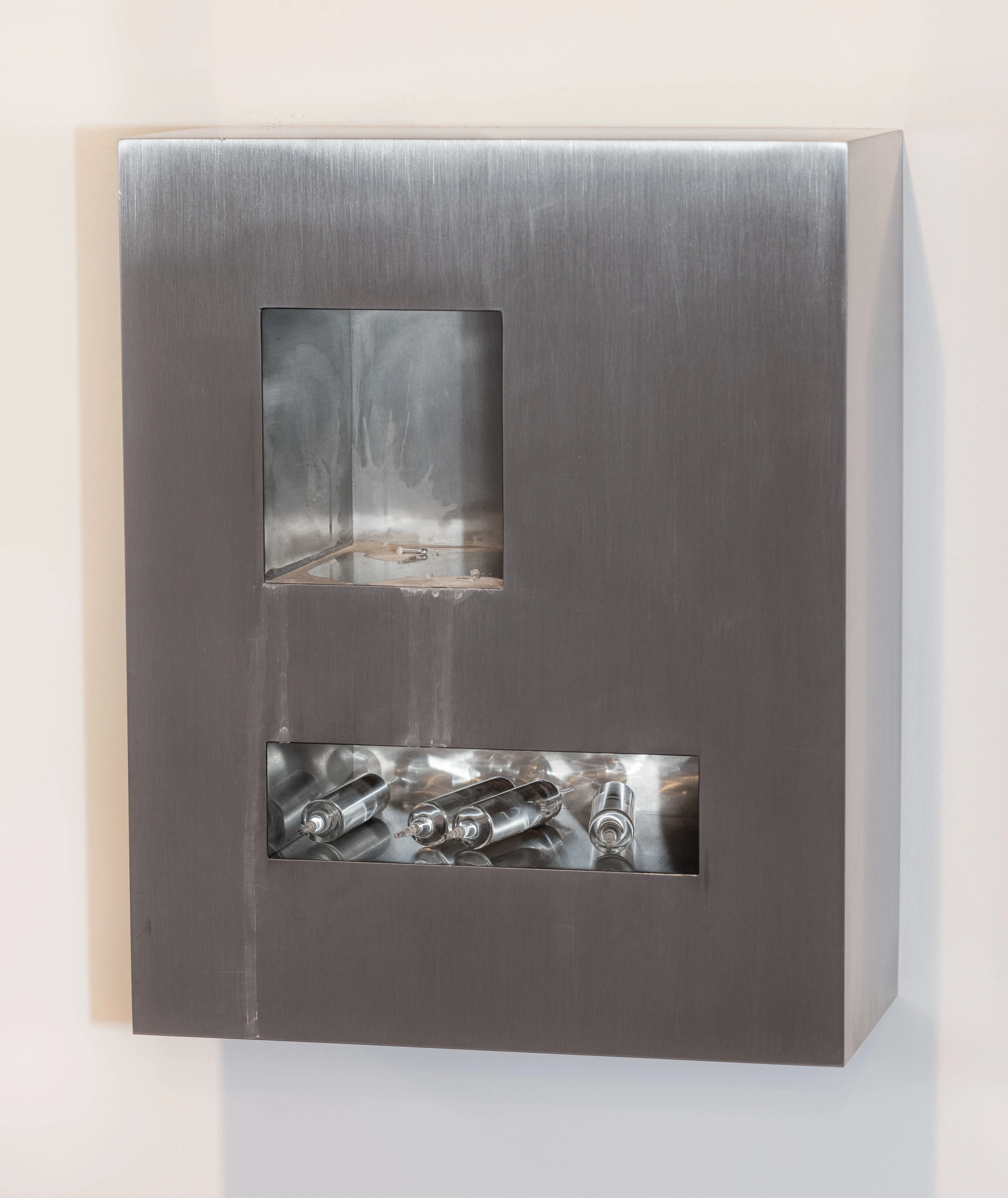 Productive Narcissism at 032c Gallery in Berlin — A brushed stainless-steel cabinet with two horizontal rectangular apertures displaying interior contents.