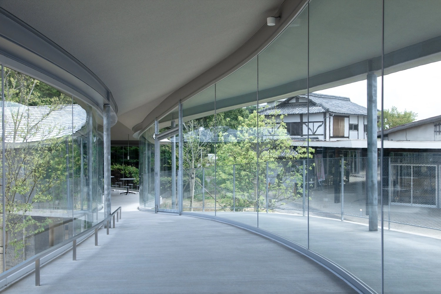 Yashima Mountaintop Park by SUO + Style-A — A glazed corridor frames the landscape beyond through floor-to-ceiling glass panels, creating a permeable threshold between interior passage and exterior...
