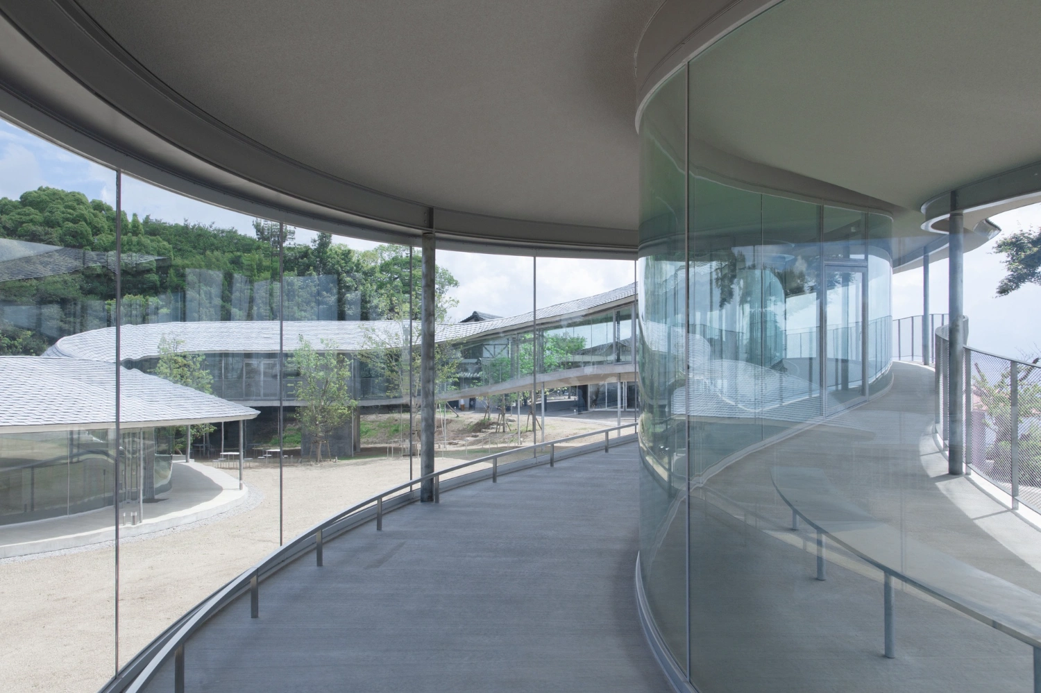 Yashima Mountaintop Park by SUO + Style-A — A curved glass corridor traces the mountaintop's contours, framing views across the landscape through floor-to-ceiling transparency.