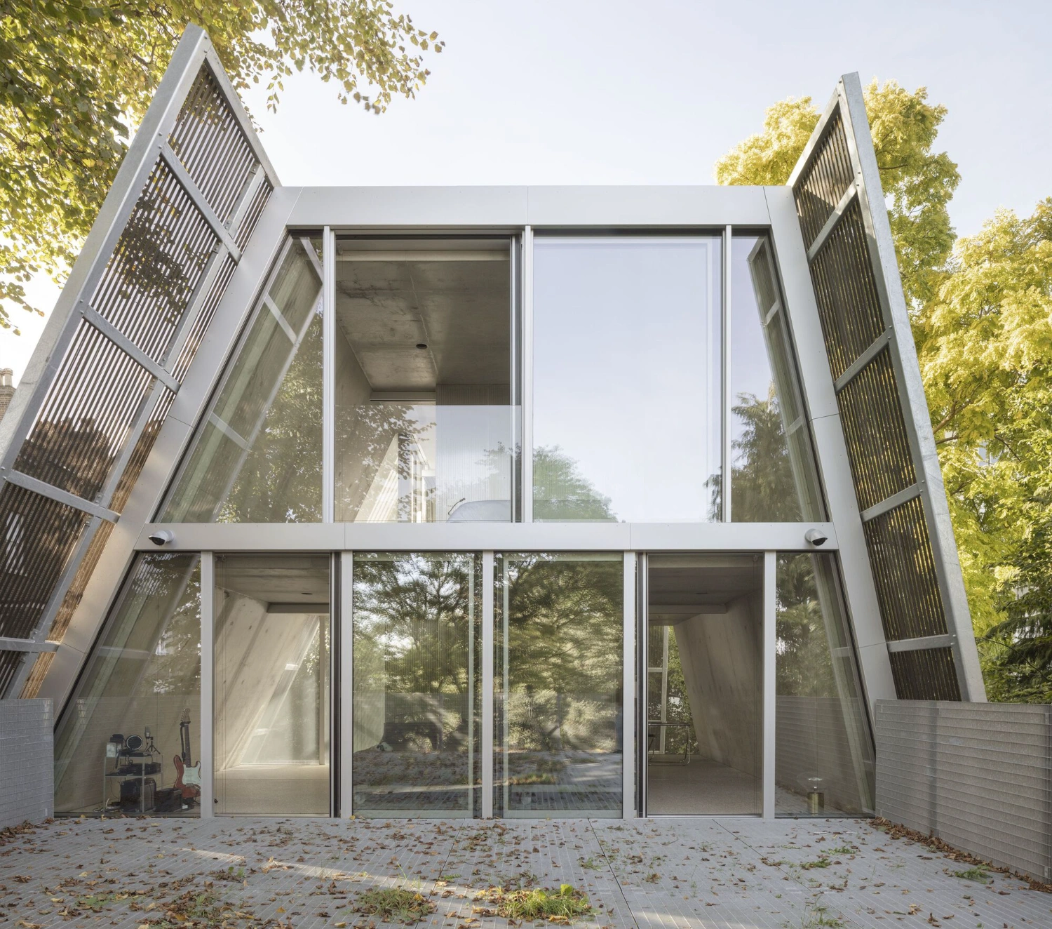 Reciprocal House by Gianni Botsford Architects — The rear facade of Reciprocal House presents a double-height glazed opening spanning the full width, with minimal aluminum framing dividing four large panes.