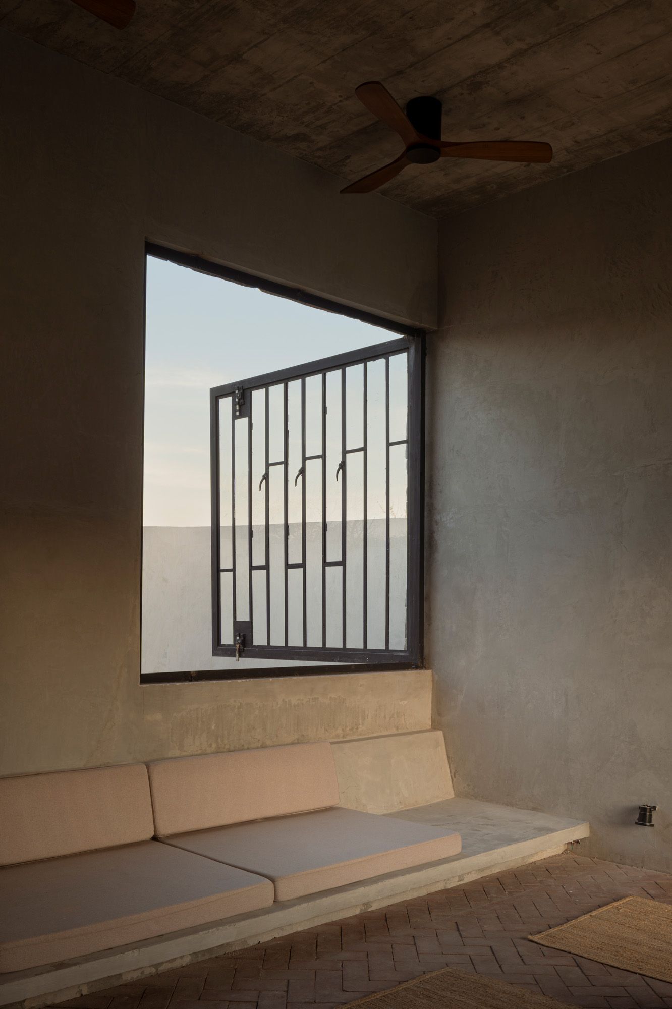 Casa La Paz by Ludwig Godefroy Architecture — A sunken interior courtyard anchors this domestic space, its recessed geometry framing a barred metal-framed window that opens onto a distant landscape.