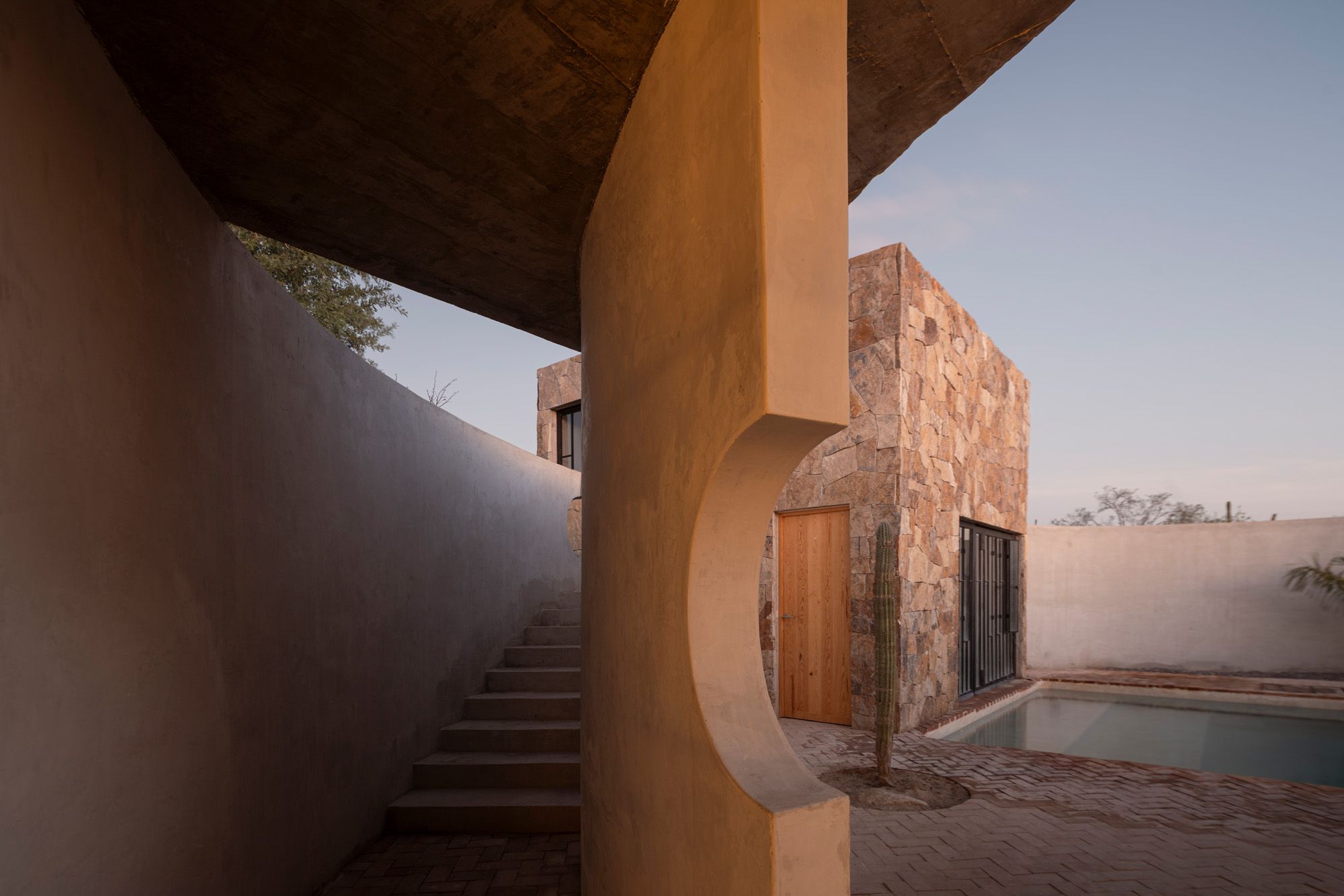 Casa La Paz by Ludwig Godefroy Architecture — A cantilevered concrete slab extends dramatically over the lower volume, creating a deep shadow across the staircase passage.