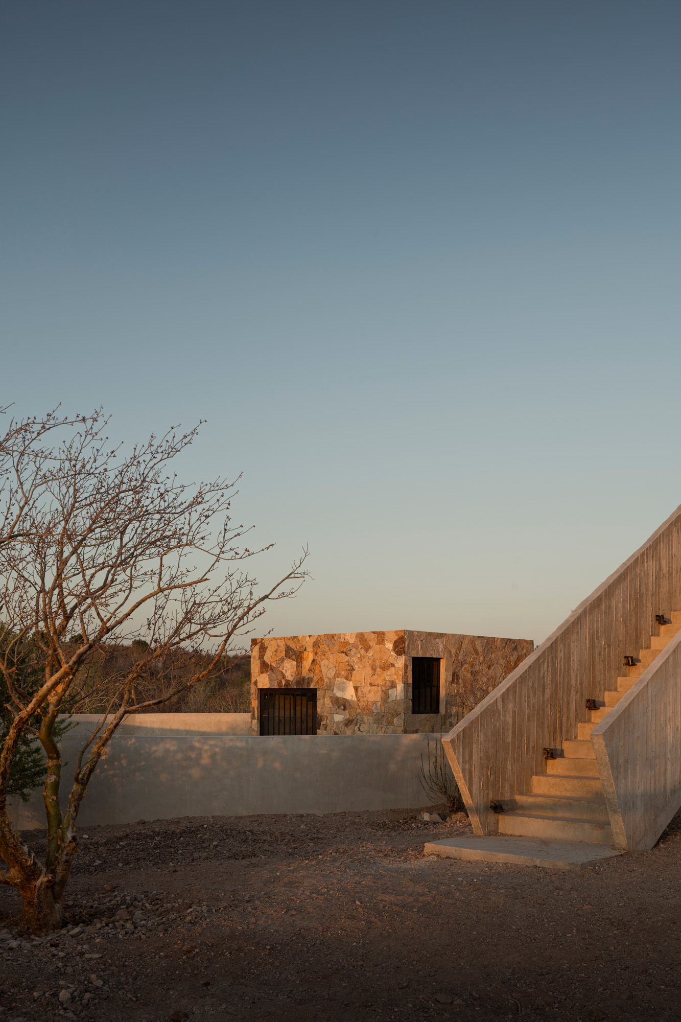 Casa La Paz by Ludwig Godefroy Architecture — Golden-hour light bathes the east-facing courtyard elevation, articulating the stacked volumetric composition through dramatic shadow geometry.