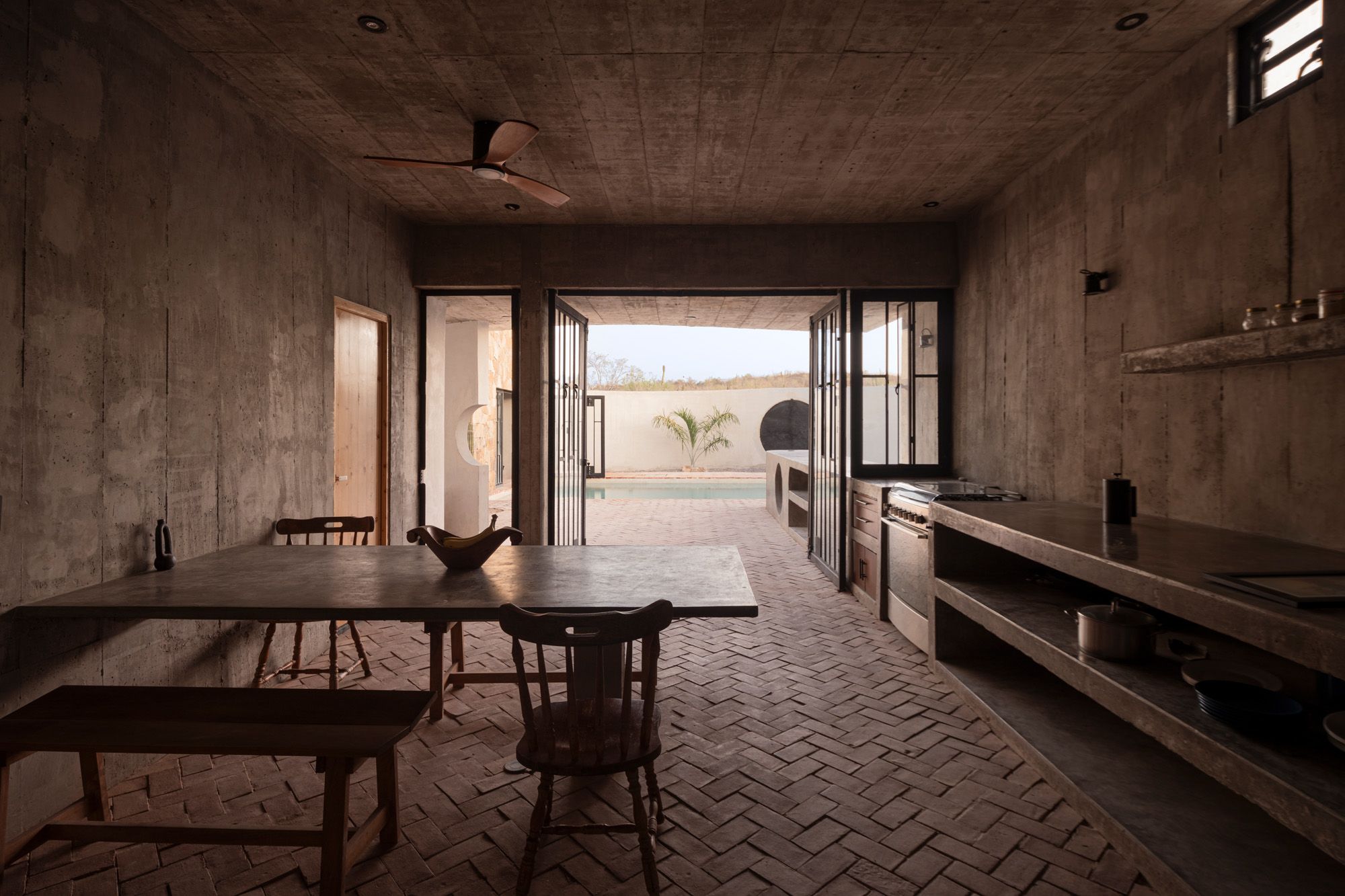 Casa La Paz by Ludwig Godefroy Architecture — The kitchen-dining interior opens directly onto the courtyard through folding glass doors, collapsing the boundary between indoor and outdoor space.