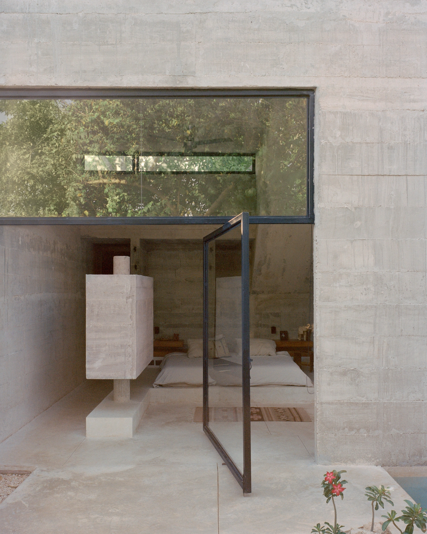 House in Los Cocos by Ludwig Godefroy Architecture — A frameless glass threshold opens onto a minimal courtyard where exposed concrete columns and walls establish a rhythmic spatial composition.