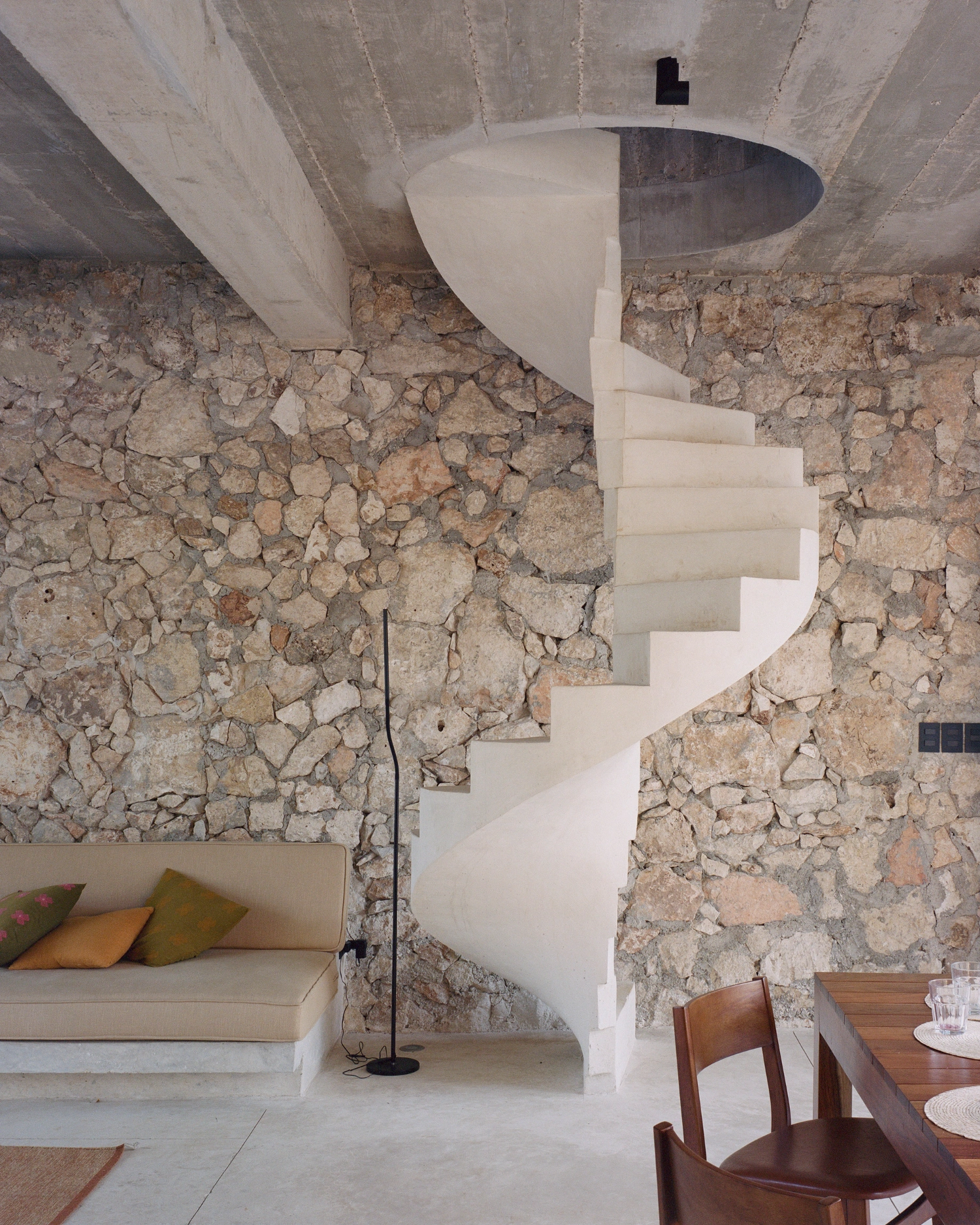 House in Los Cocos by Ludwig Godefroy Architecture — A sculptural spiral staircase in white concrete anchors the interior space, its cantilevered steps ascending toward an opening in the ceiling.