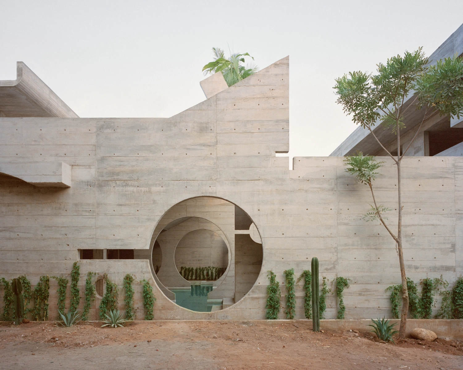 House TO by Ludwig Godefroy Architecture — A monolithic concrete facade dominates the composition, its surface revealing board-formed casting marks and pour lines.