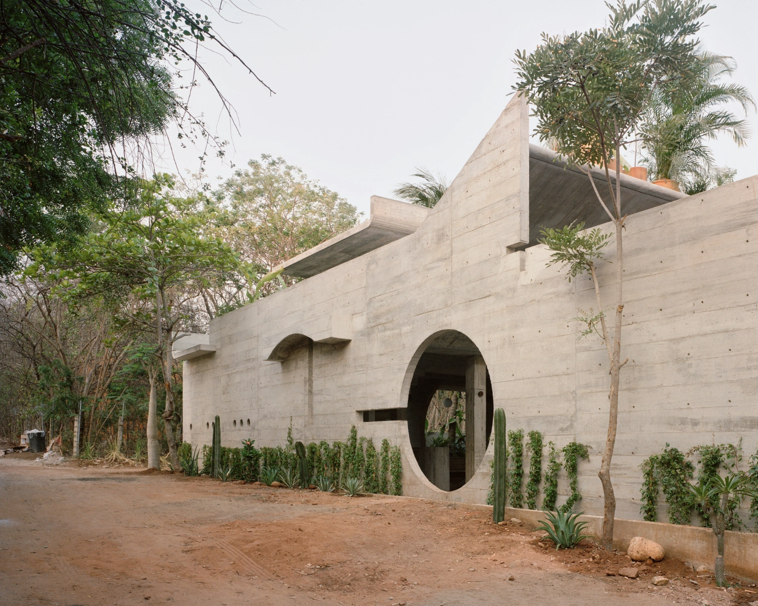 House TO by Ludwig Godefroy Architecture — House TO's monolithic concrete facade presents a sculptural composition of curved voids and cantilevered planes.