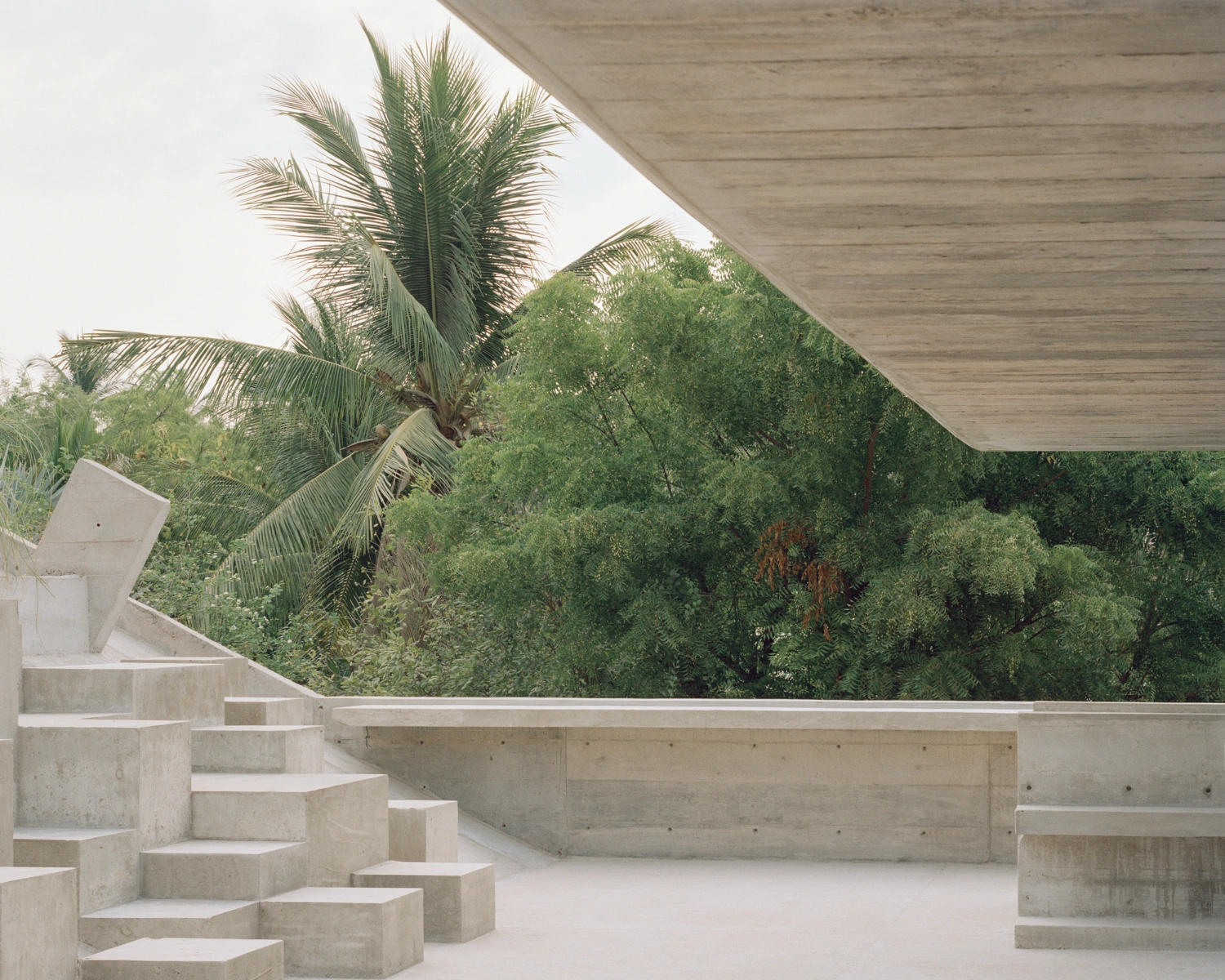 House TO by Ludwig Godefroy Architecture — A concrete terrace frames a verdant landscape through a geometric aperture, the building's monolithic form contrasting sharply with dense tropical vegetation.