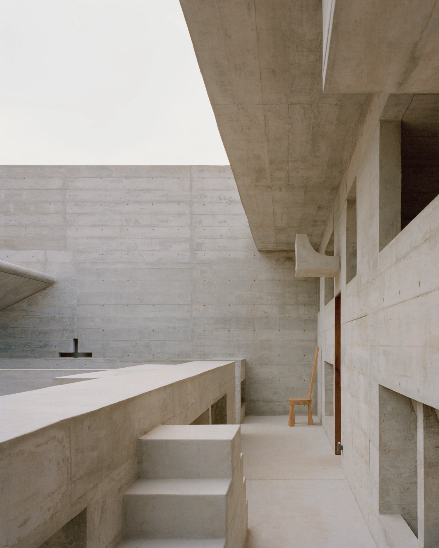 House TO by Ludwig Godefroy Architecture — A poured-concrete interior passage frames brutalist spatial geometry through board-formed walls revealing construction seams.