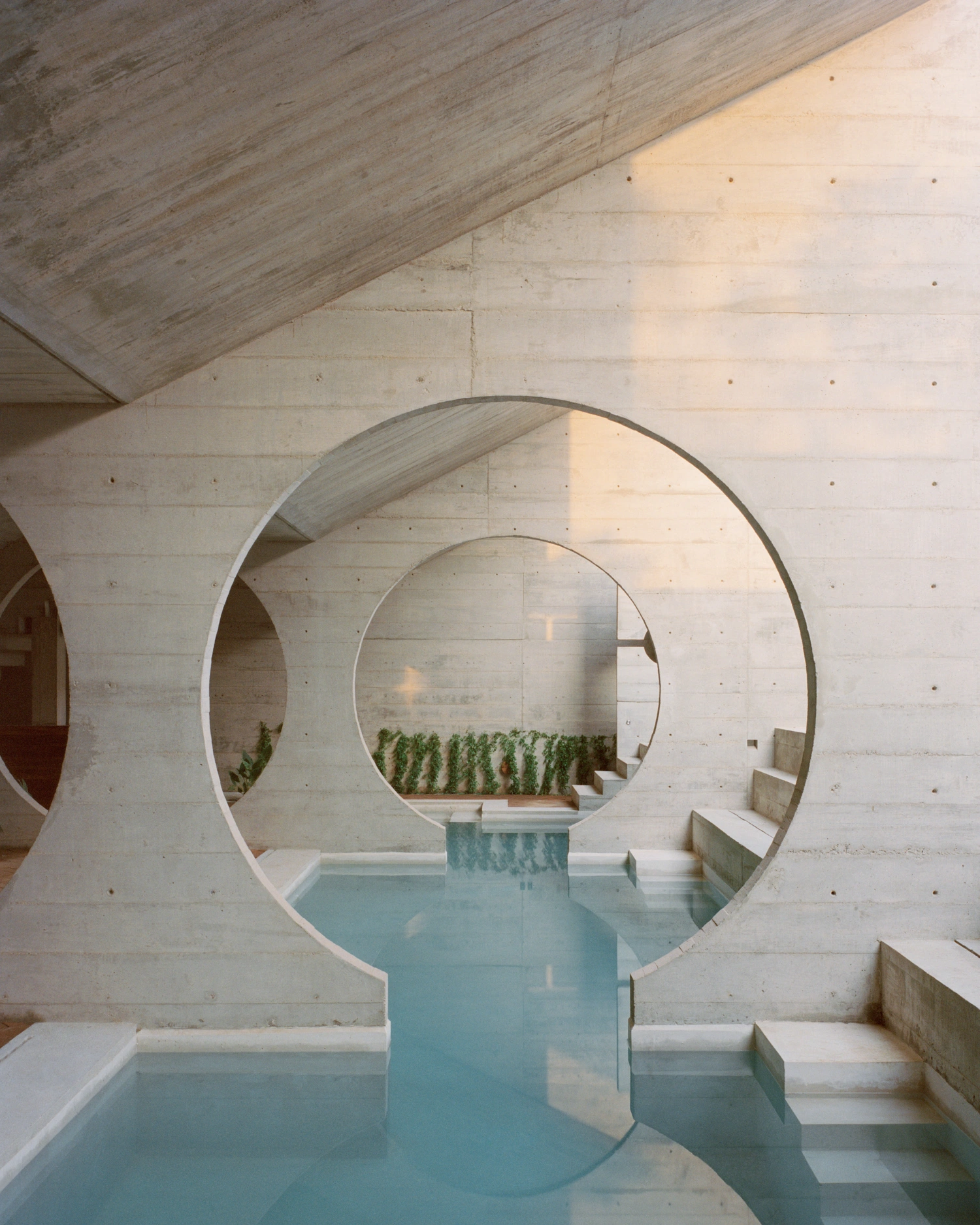 House TO by Ludwig Godefroy Architecture — A monolithic concrete structure frames nested circular voids that create tunnel-like depth into the interior courtyard.