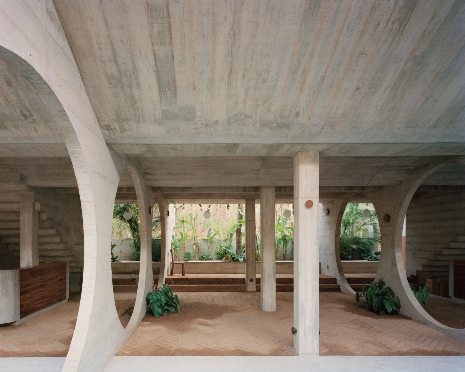 House TO by Ludwig Godefroy Architecture — Concrete colonnade framing a central courtyard planted with green vegetation.