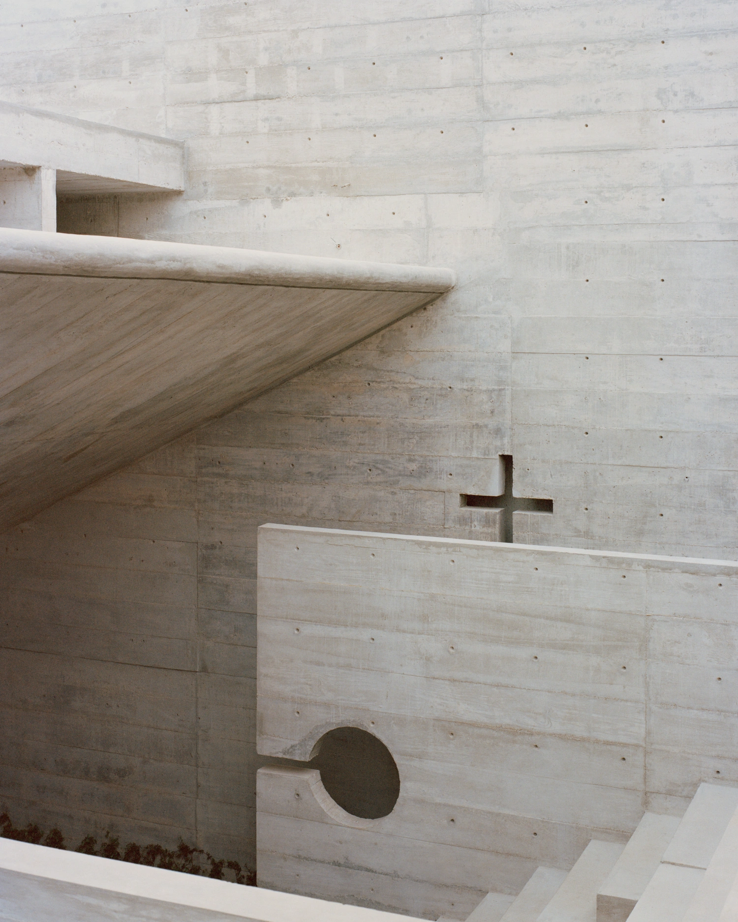 House TO by Ludwig Godefroy Architecture — A view into House TO's interior reveals a monolithic concrete wall with a large circular void opening, its edges softened by concentric curved surfaces...