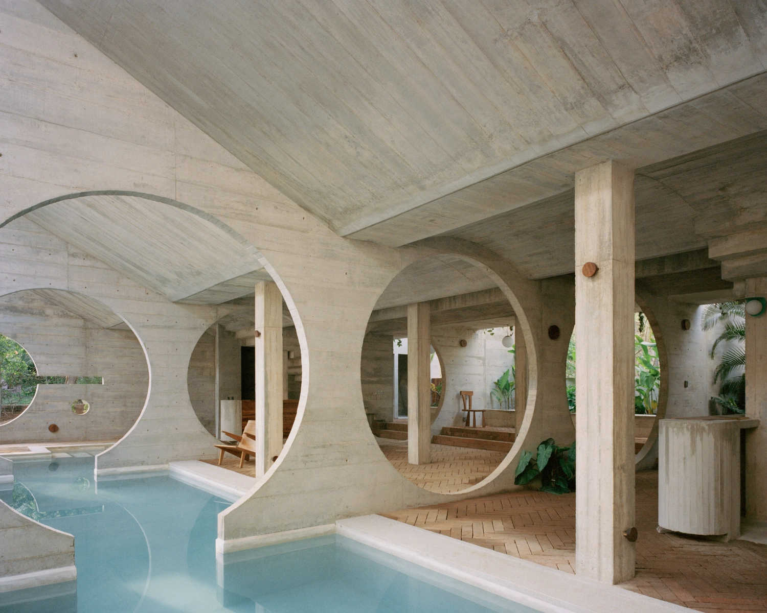 House TO by Ludwig Godefroy Architecture — A monolithic concrete structure frames successive circular voids that tunnel through the building's depth, creating layered sightlines toward interior spaces.