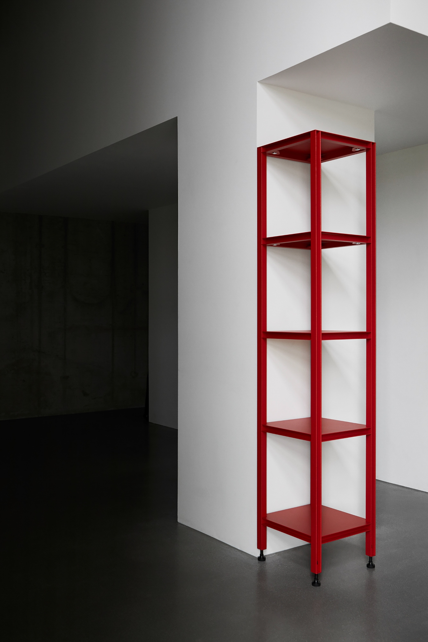 Full Metal by Matteo Bauer-Bornemann — A tall narrow shelving unit constructed from powder-coated steel in deep red, positioned against white architectural walls.
