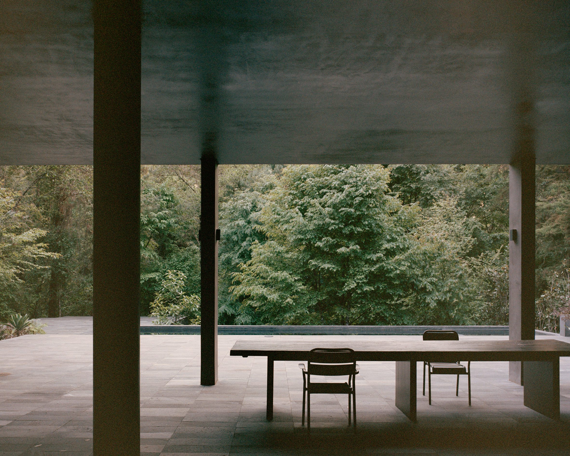 Copas House by PPAA — A cantilevered concrete platform extends into forest canopy, framed by two massive cylindrical columns supporting an overhead soffit.