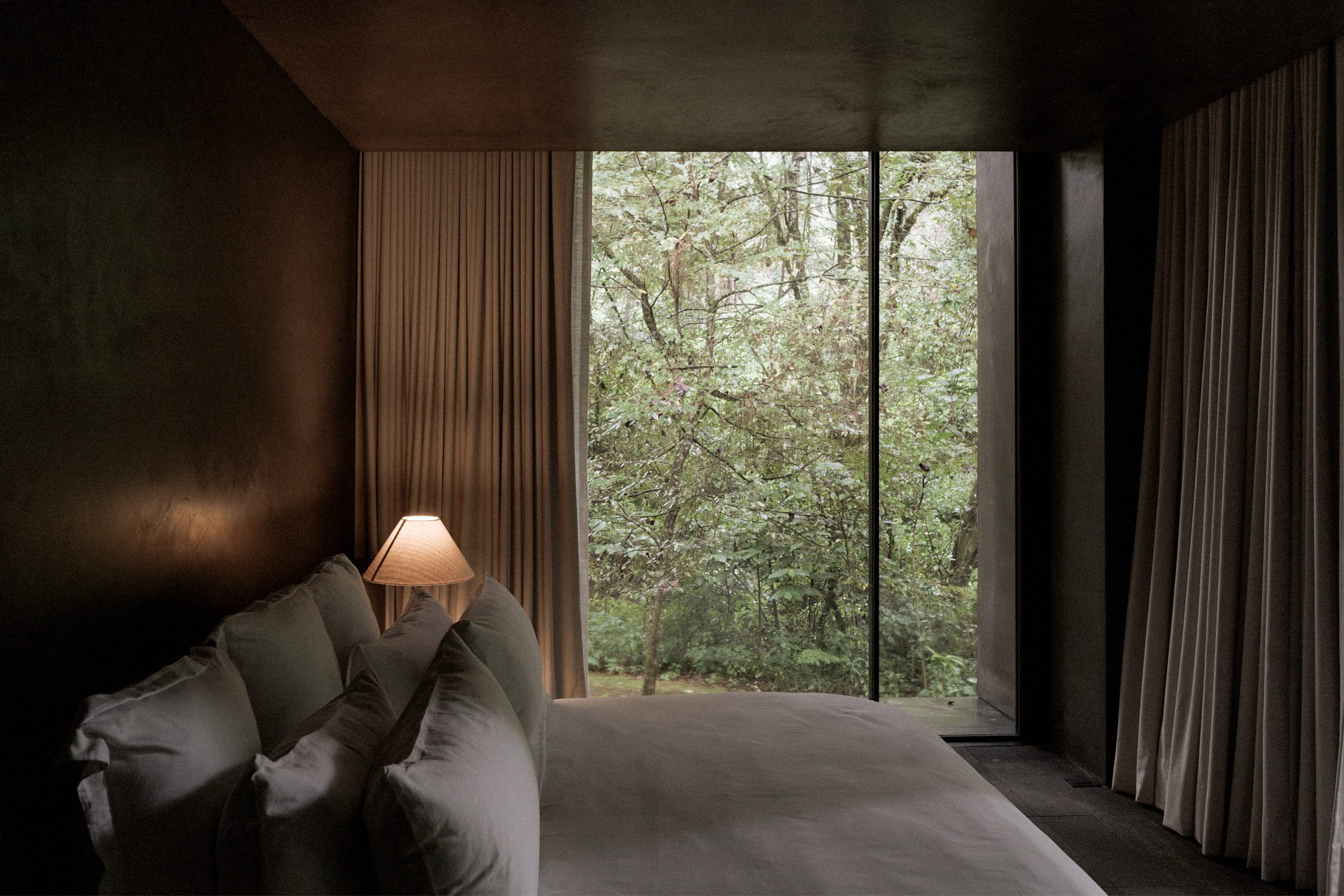 Copas House by PPAA — A bedroom interior frames the forest through floor-to-ceiling glazing, where deciduous trees occupy the entire visual field.
