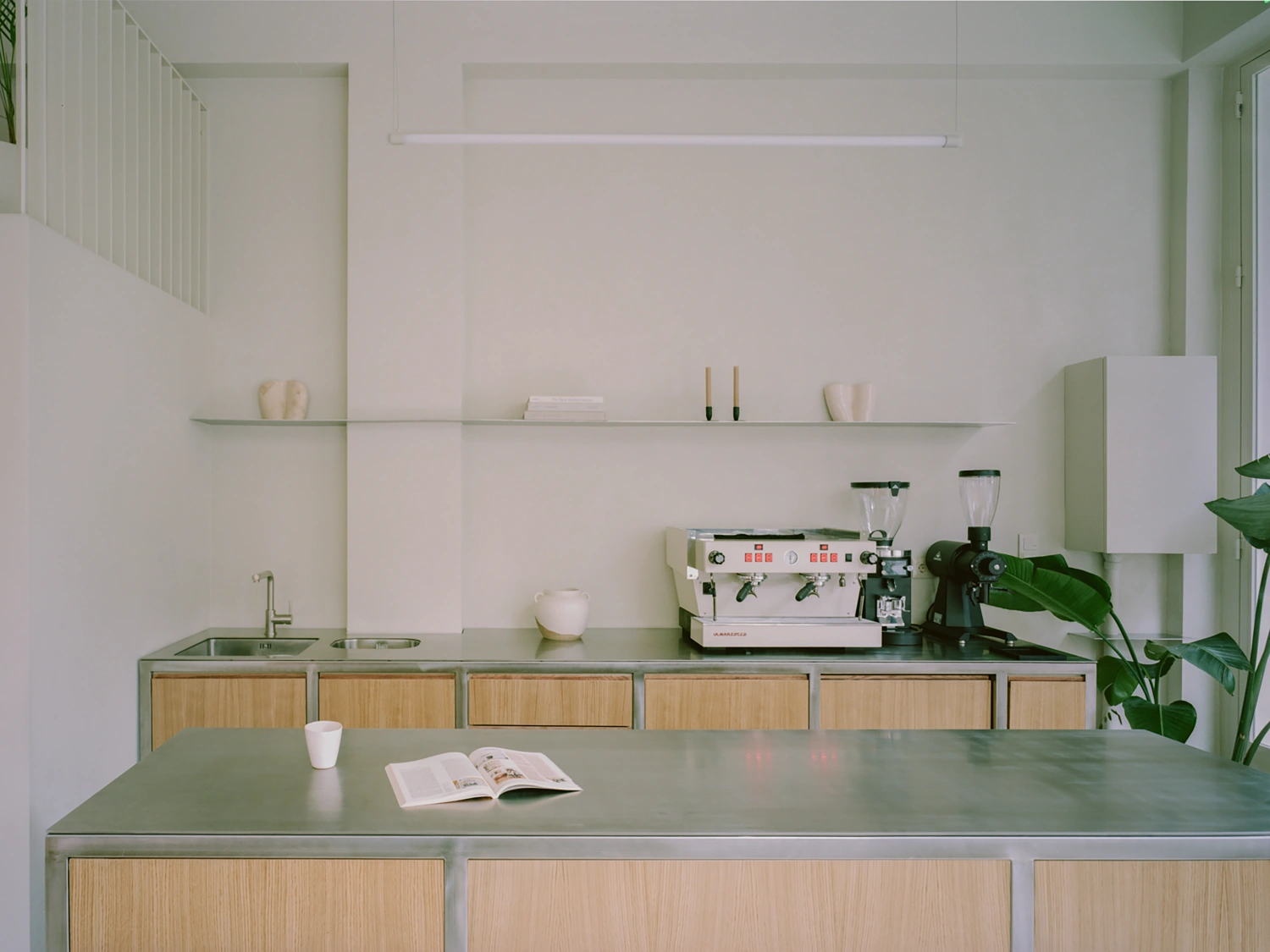 Moden Café by Georgios Apostolopoulos — The café counter anchors the ground-floor interior with a bespoke oak base topped by sage-green metal, stretching the full width of the space.