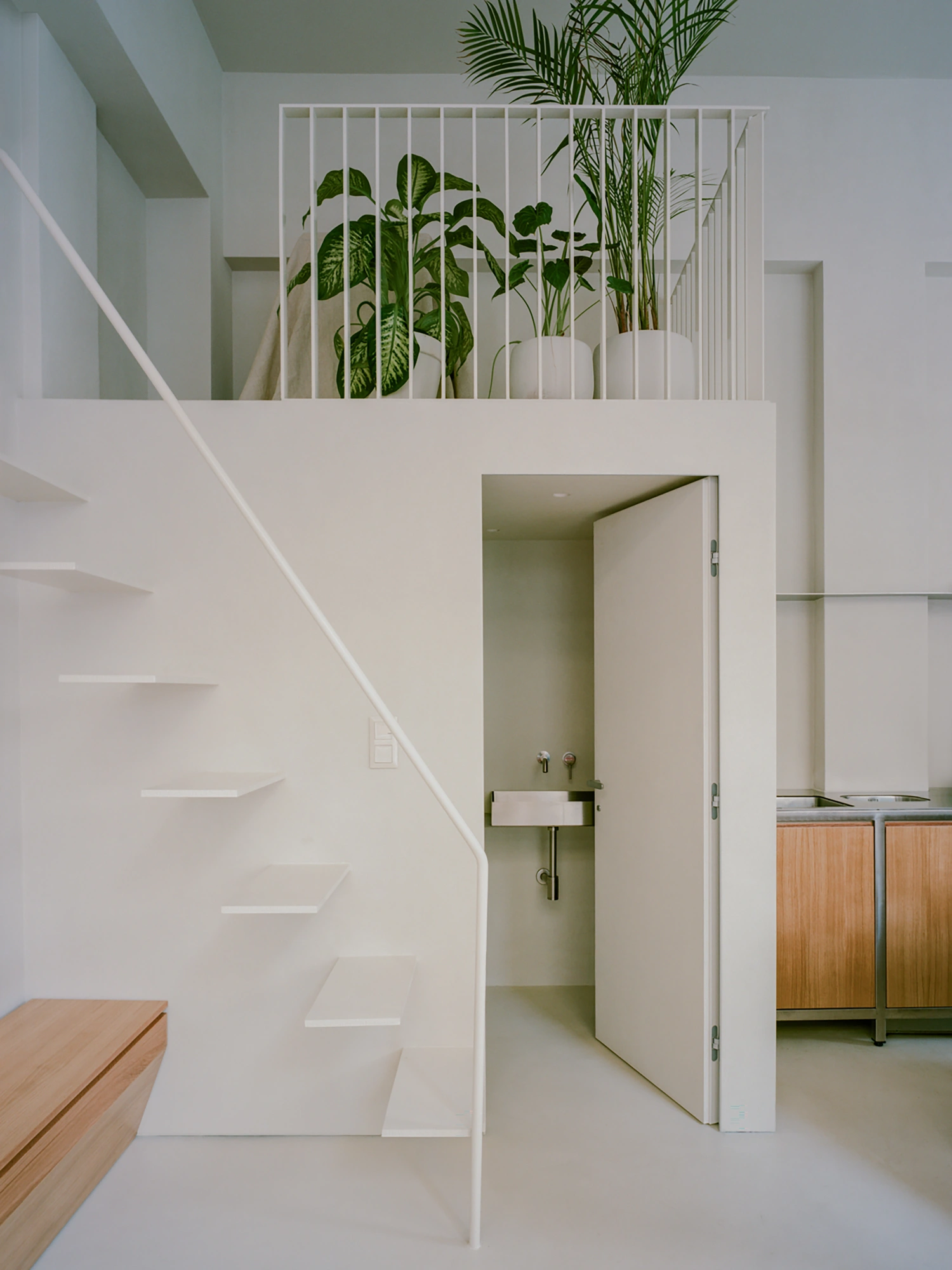 Moden Café by Georgios Apostolopoulos — A staircase with floating white steps ascends the left wall, its geometry contrasting sharply against the cream plaster.