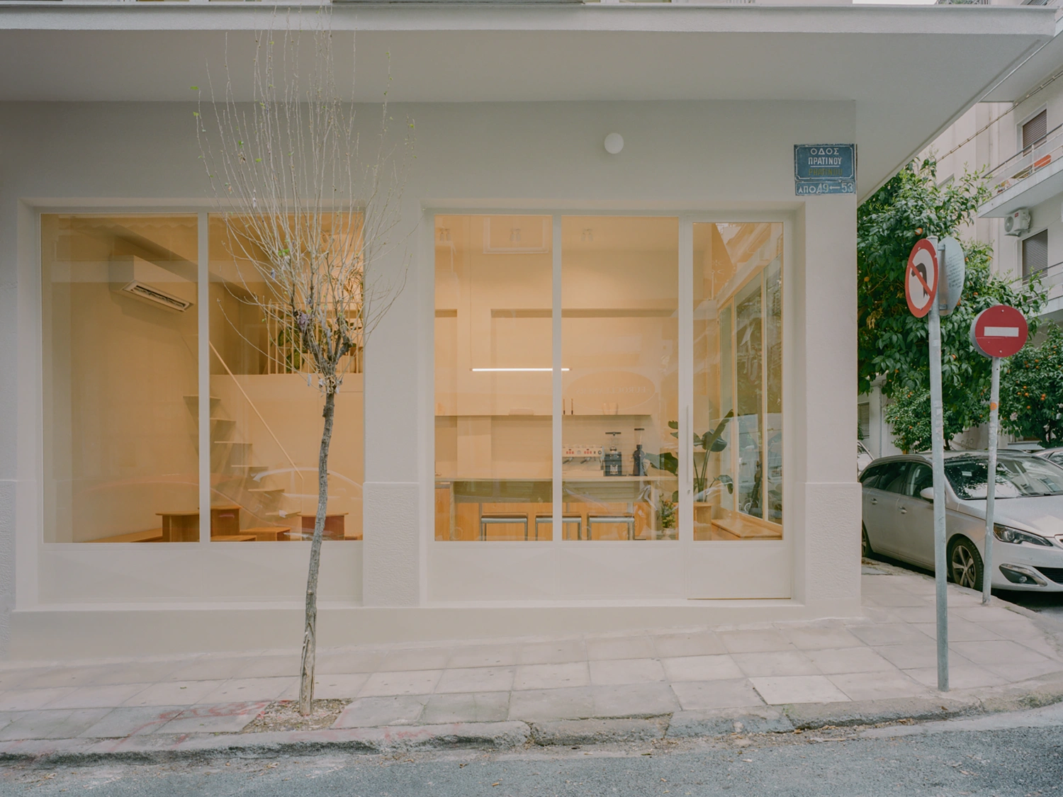 Moden Café by Georgios Apostolopoulos — The storefront elevation presents a floor-to-ceiling glazed facade with white aluminum framing, revealing the cafe's minimalist interior.