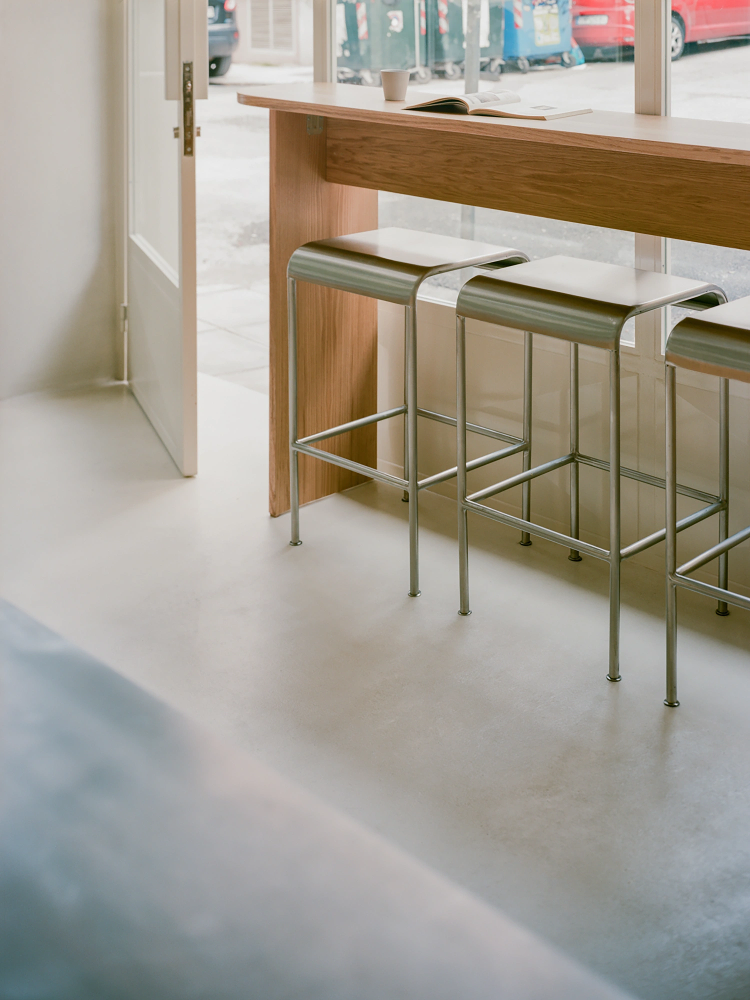 Moden Café by Georgios Apostolopoulos — The café interior is anchored by a bespoke oak counter with integrated metal bar seating in sage-green and cream.