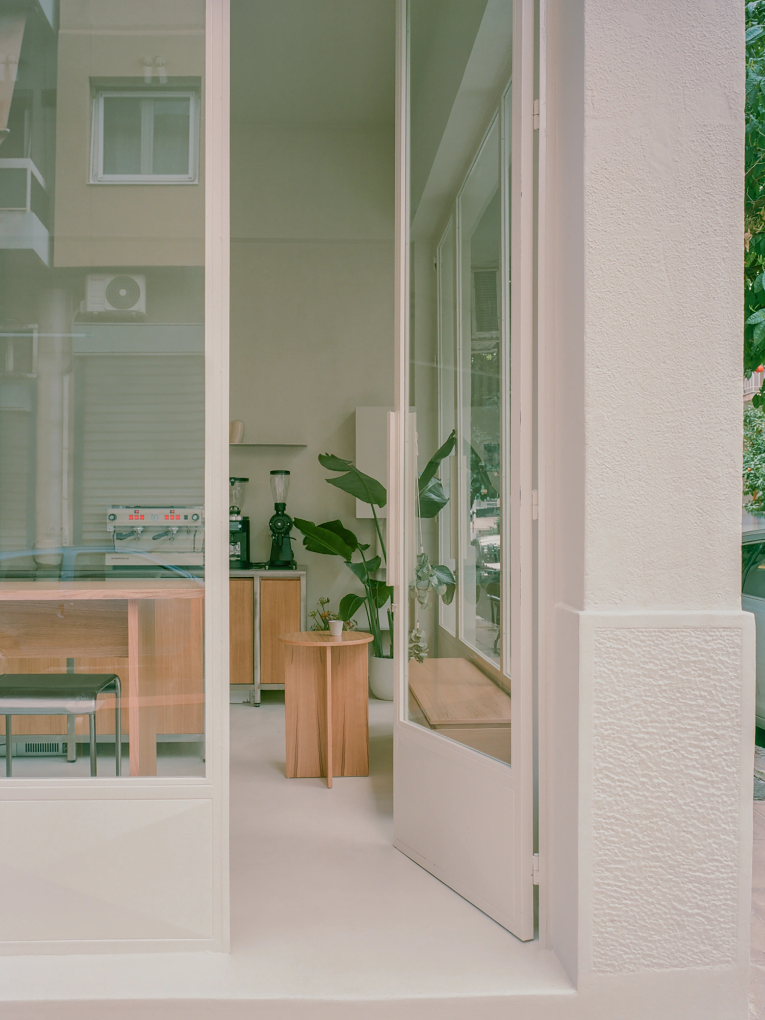 Moden Café by Georgios Apostolopoulos — A threshold view into Moden Café reveals layered spatial depth through floor-to-ceiling glazing with white aluminum framing.