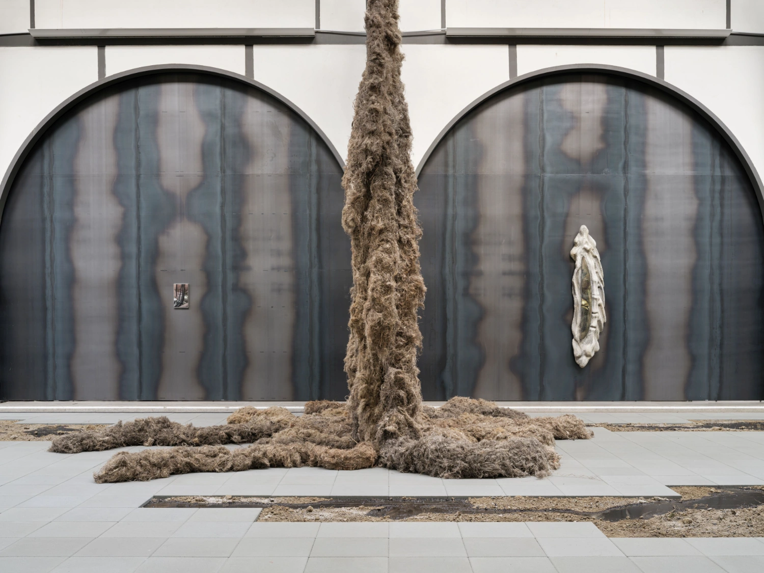 'embrace' by Klára Hosnedlová at Hamburger Bahnhof — A monumental flax column rises through the center of the gallery floor, its twisted fibrous surface in cream and rust tones anchored by scattered soil...
