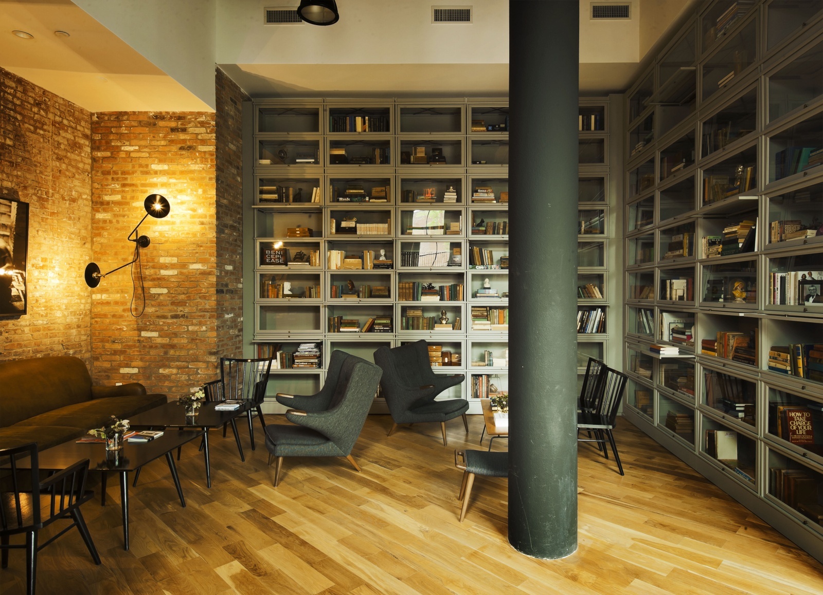 Wythe Hotel New York by Morris Adjmi Architects — A library lounge within the Wythe Hotel's preserved industrial shell, featuring floor-to-ceiling gridded glass-fronted cabinetry in sage-green steel frames...