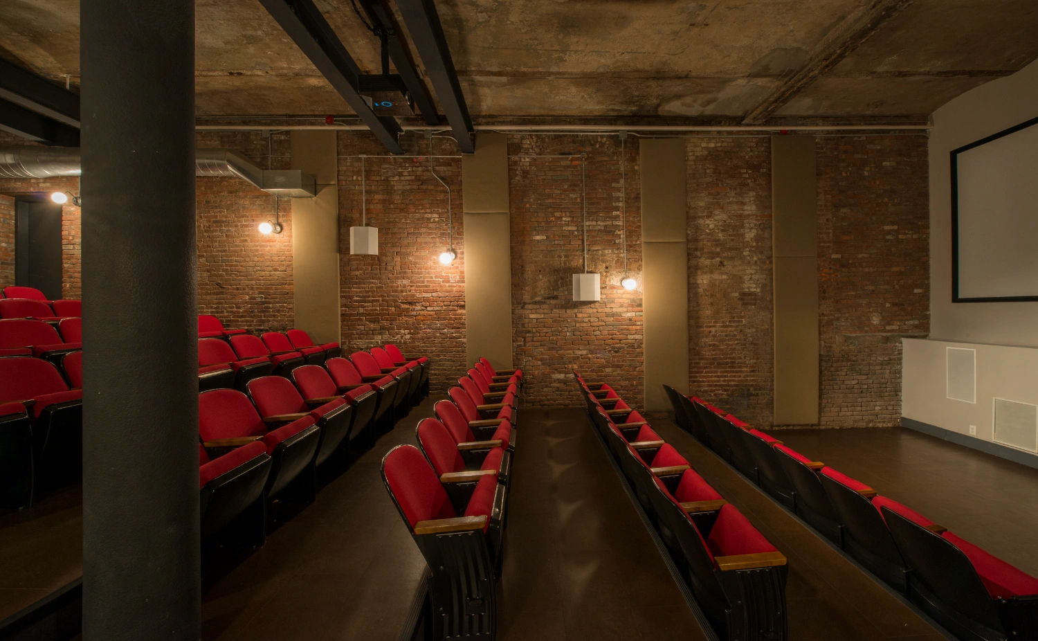 Wythe Hotel New York by Morris Adjmi Architects — A basement screening room within the preserved cooperage features three rows of burgundy theater seating arranged in rectilinear formation.
