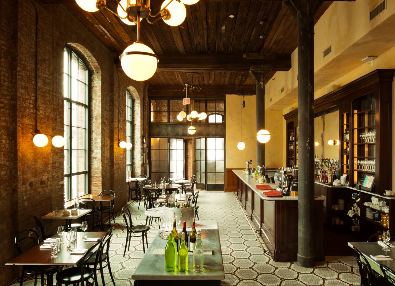 Wythe Hotel New York by Morris Adjmi Architects — The dining room extends as a linear corridor beneath a timber-slat ceiling punctuated by spherical pendant lights in brass.