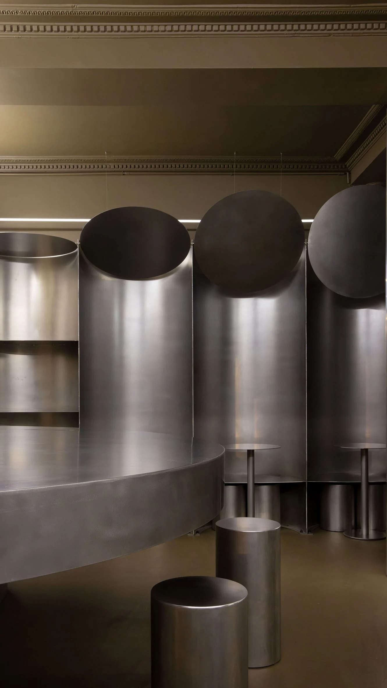 Simple Coffee by Mur Mur Architects — A monolithic interior volume defined by brushed stainless steel surfaces and cylindrical volumetric elements.