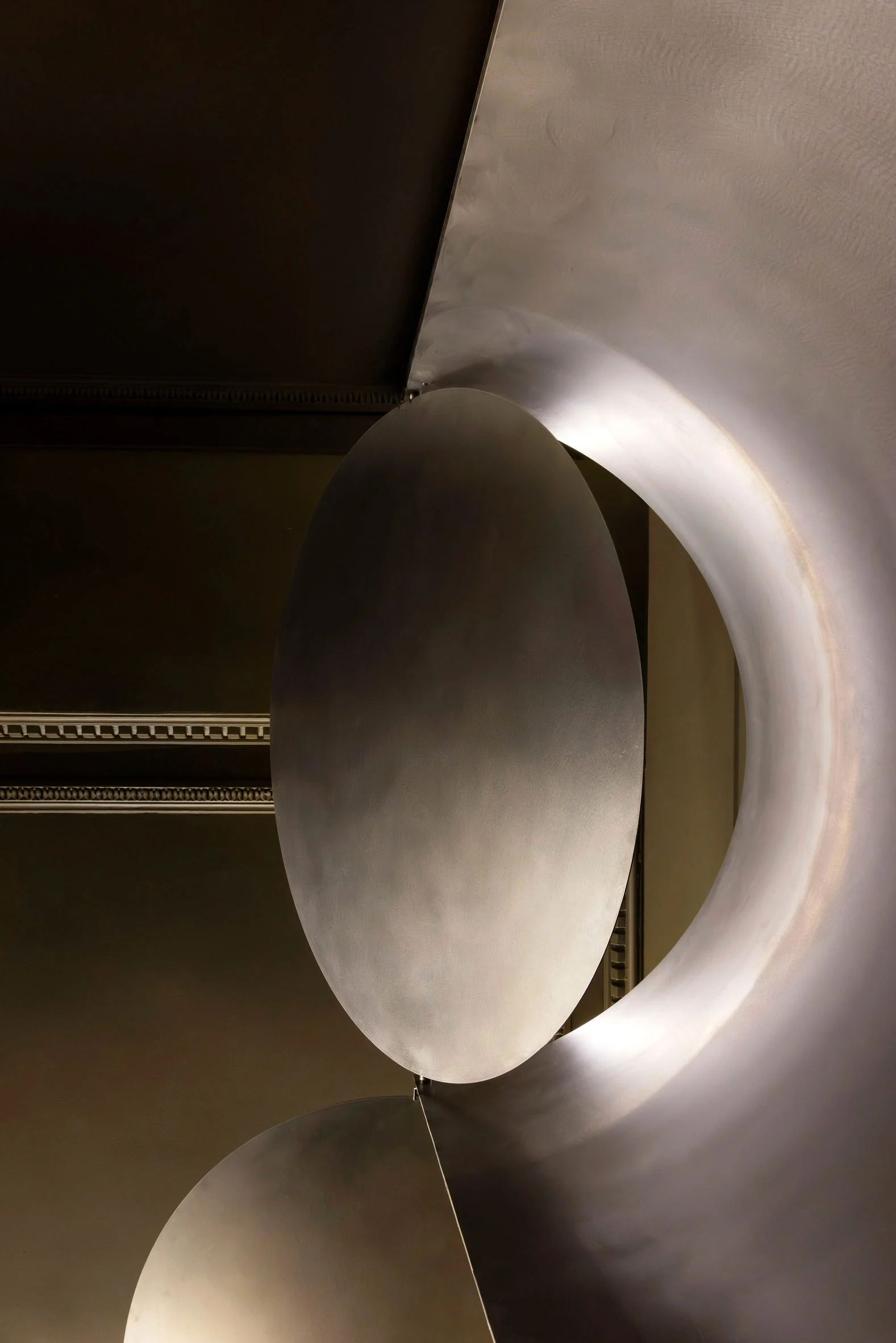 Simple Coffee by Mur Mur Architects — A close-up photograph isolates a cylindrical steel seating element in foreground, its brushed surface catching directional light that creates sharp shadow...