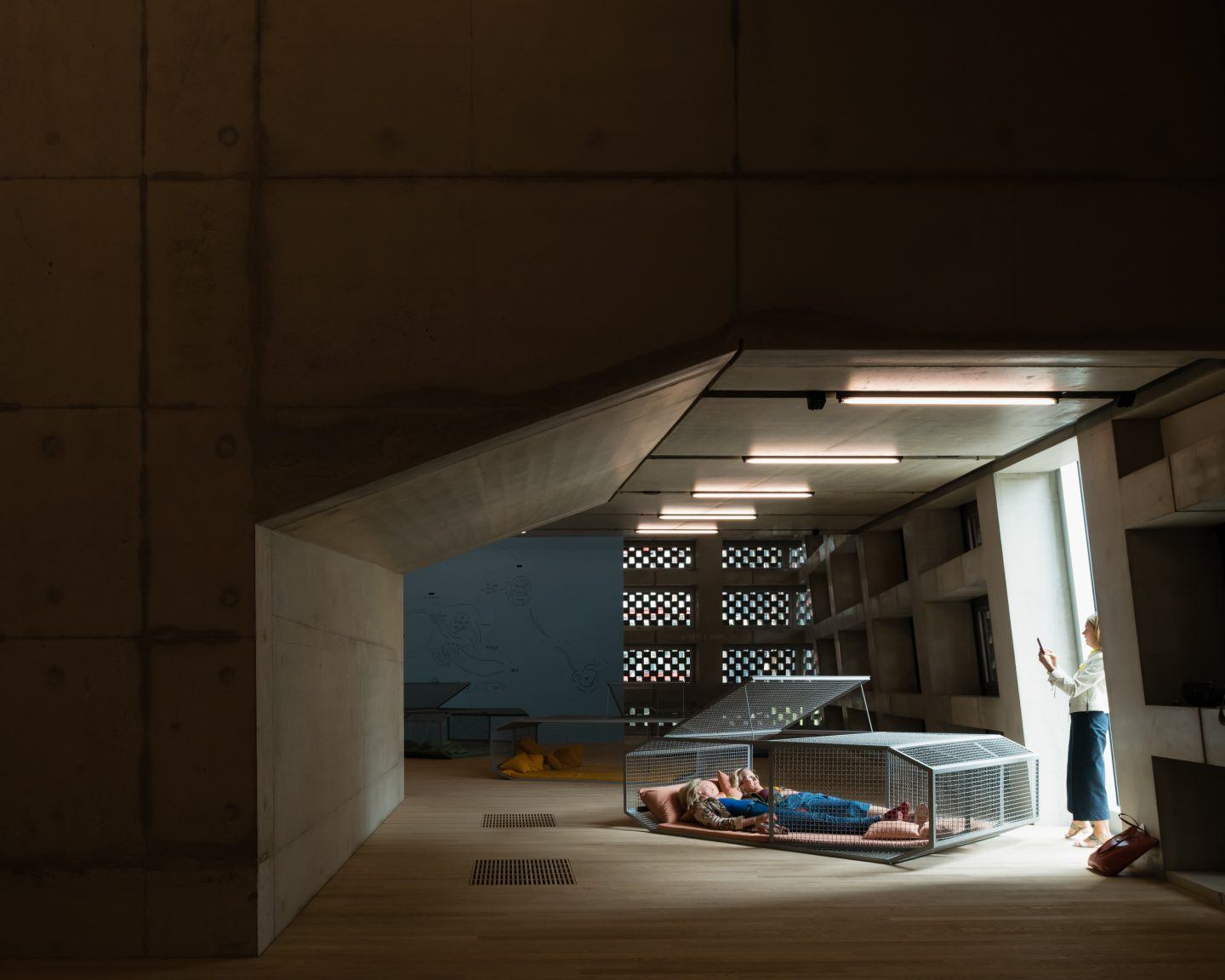 The Tate Modern by Herzog & de Meuron — A figure reclines within a mesh-enclosed structure on the polished concrete floor of the Tate Modern's cavernous interior.