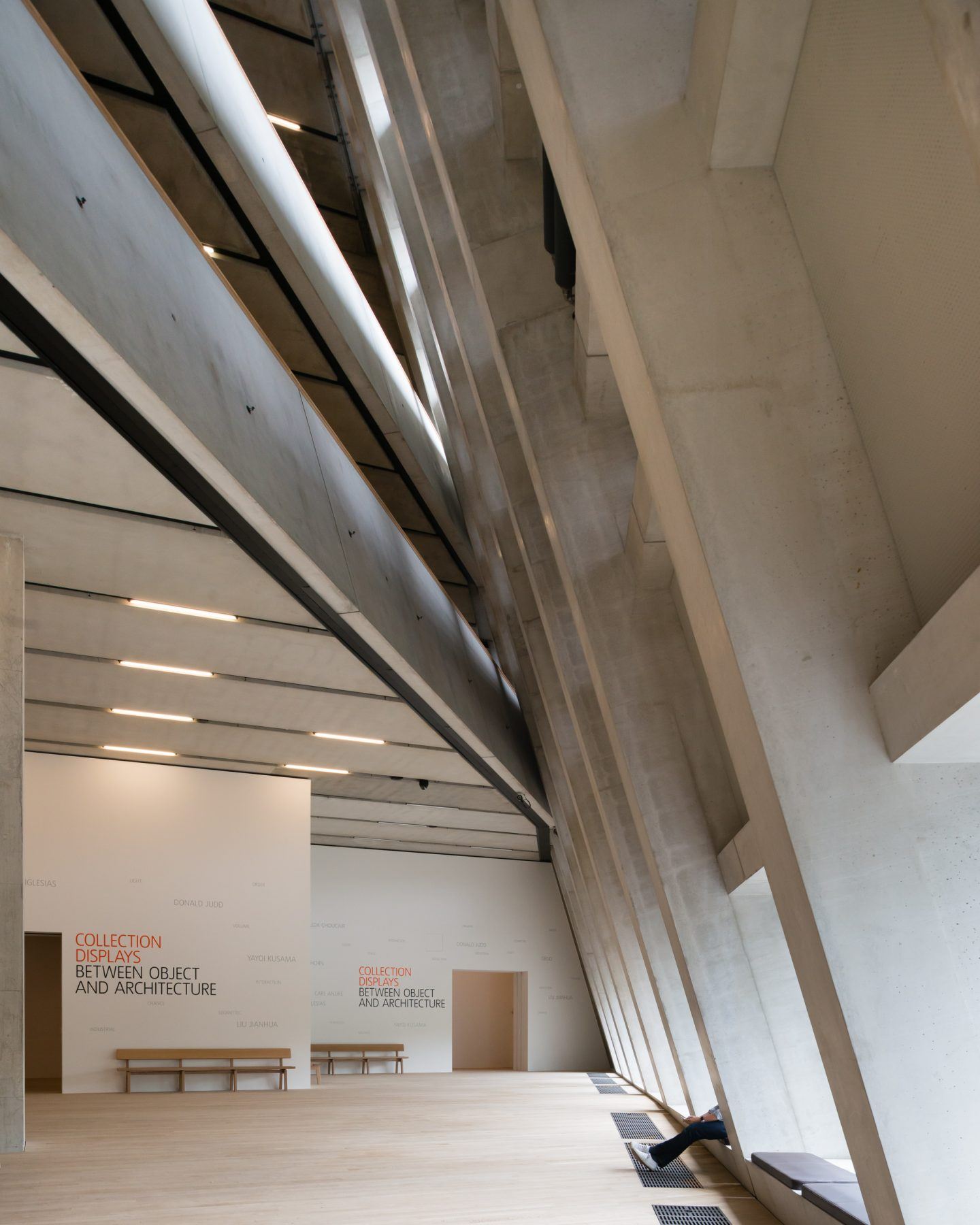 The Tate Modern by Herzog & de Meuron — The upper gallery interior reveals Herzog & de Meuron's intervention through layered ceiling planes and sculptural concrete beams that cut diagonally across...