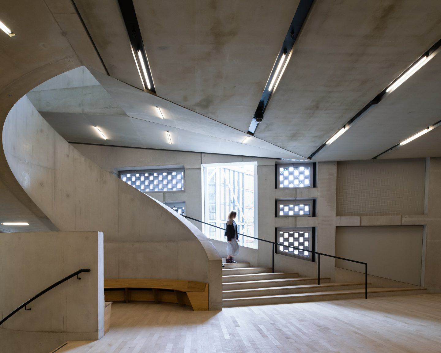 The Tate Modern by Herzog & de Meuron — A multi-level interior staircase lit by linear fluorescent ceiling panels that emphasize the horizontal plane of the concrete structure.