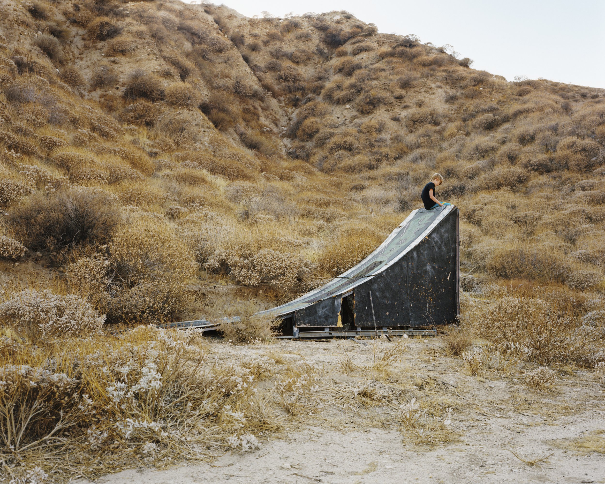 A Poor Sort of Memory by Tracy L Chandler — A weathered steel slide structure with oxidized patina sits at an oblique angle against a California desert hillside densely covered in sage-toned scrub brush.
