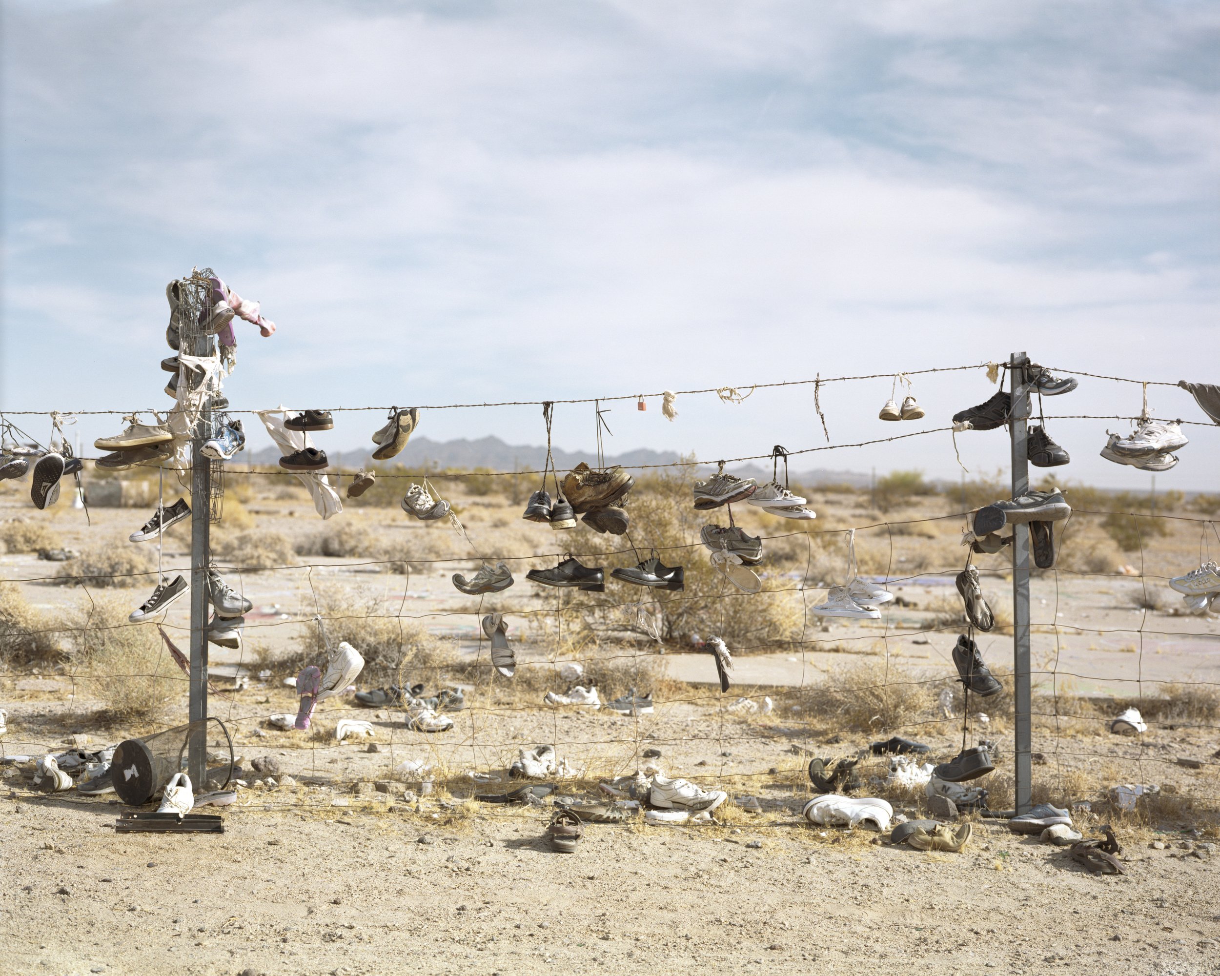 A Poor Sort of Memory by Tracy L Chandler — Shoes dangle from wire strung between two wooden posts across a desert wasteland, a found-object installation embedded in the California landscape.