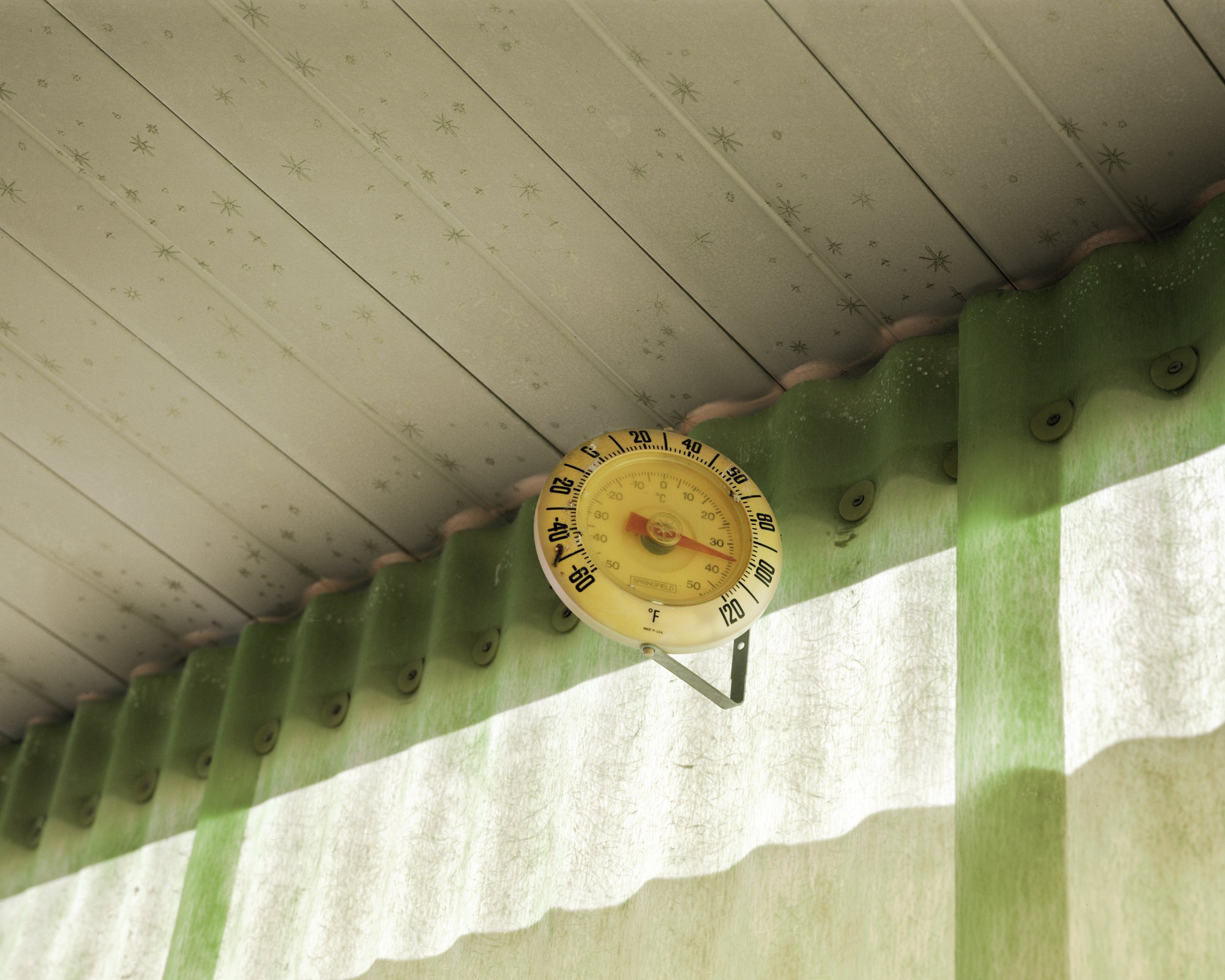 A Poor Sort of Memory by Tracy L Chandler — A vintage thermometer mounted on weathered green corrugated metal reads approximately 50 degrees Fahrenheit.