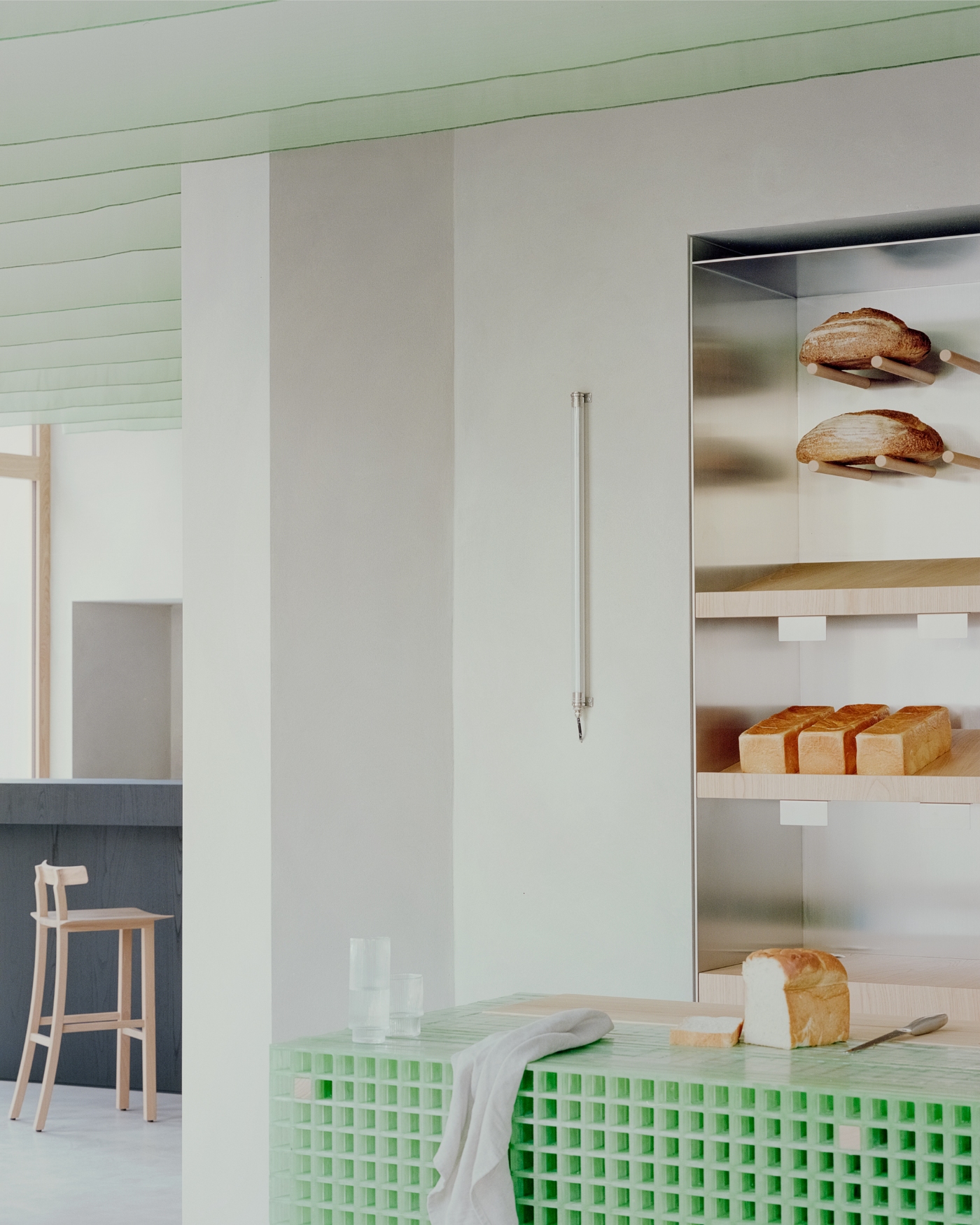 PAN Milano by studio wok — A bakery counter fronted with green fiberglass grating that glows softly under overhead light.