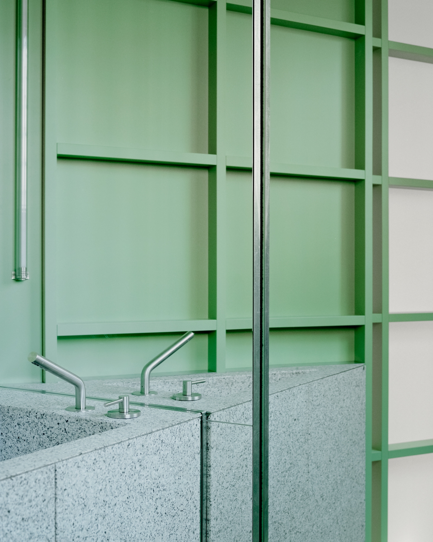 PAN Milano by studio wok — A close-up view of PAN Milano's bathroom threshold, where a gray terrazzo counter with embedded aggregate meets a gridded green fiberglass partition.