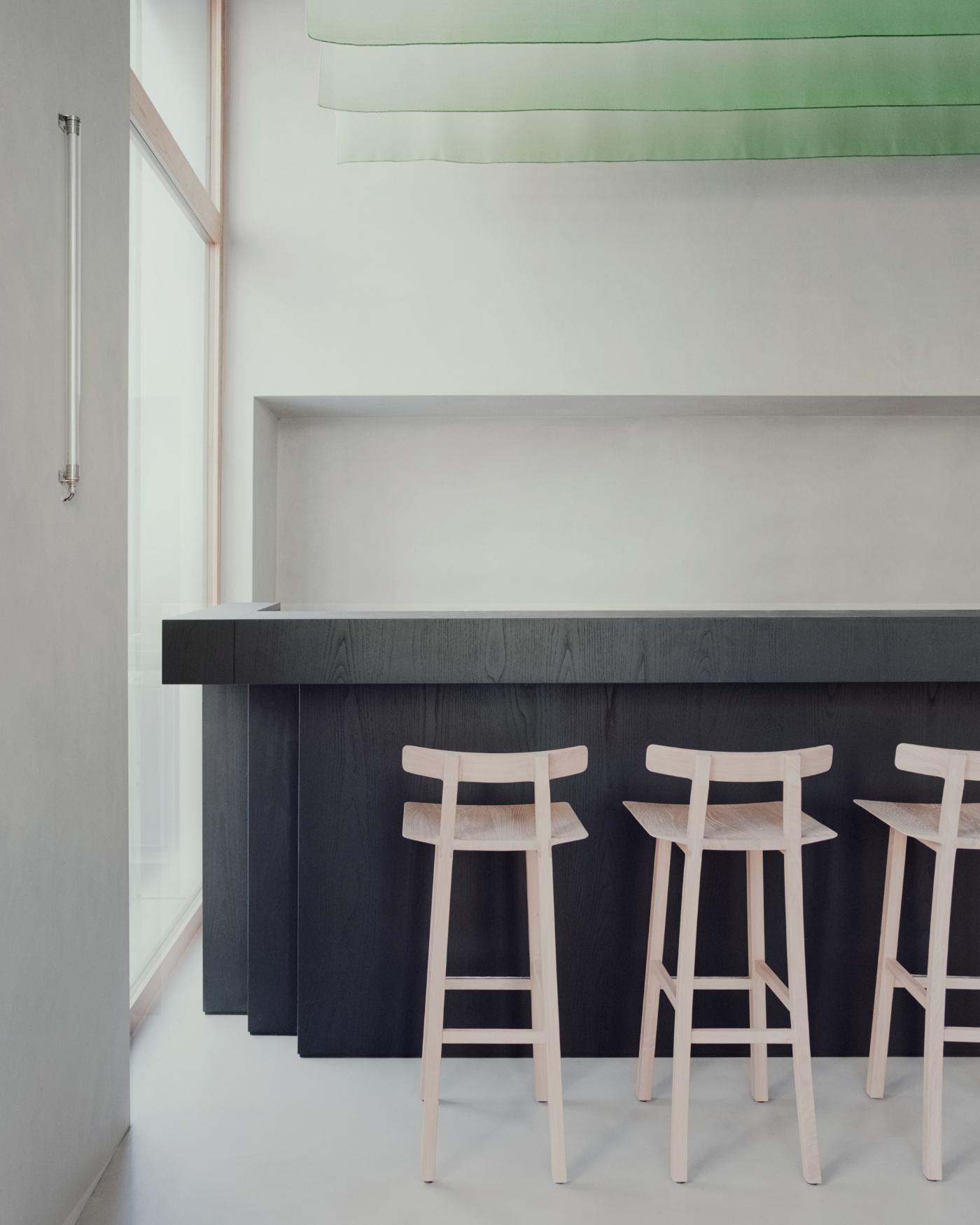 PAN Milano by studio wok — A kitchen counter in dark-stained timber anchors the composition, its substantial horizontal plane cantilevered to create an uninterrupted line.