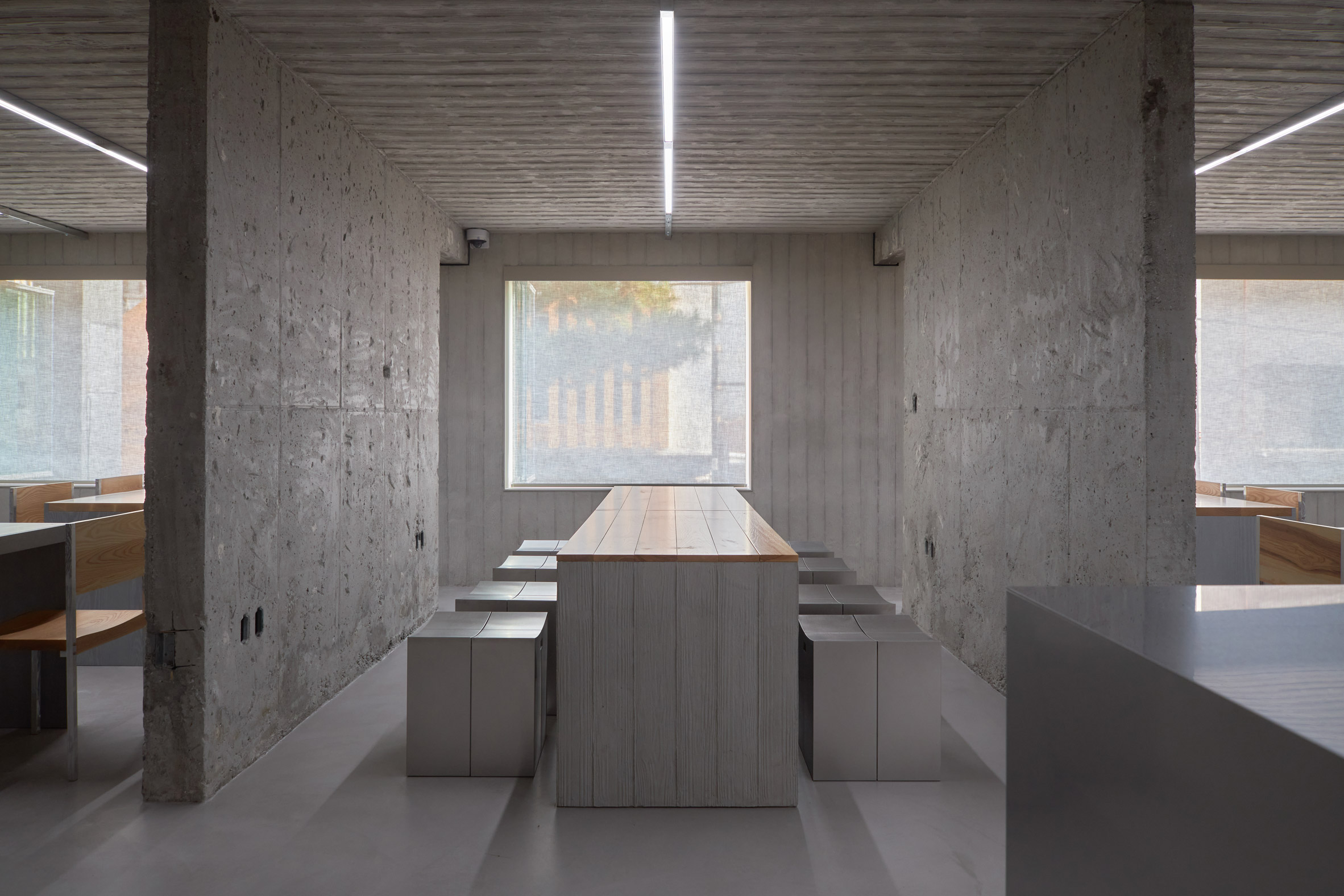 HAHOUSE Cafe by Niceworkshop — A linear corridor defined by symmetrical concrete columns and stainless steel walls etched with wood-grain texture.