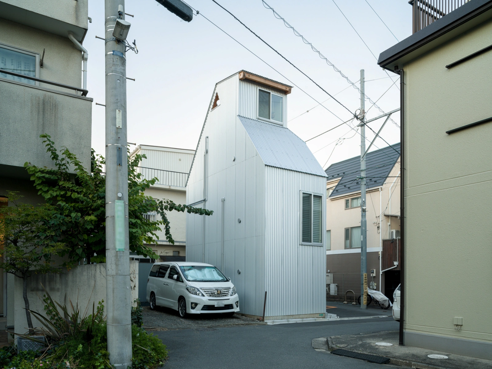Small House on a Corner Lot by KOMINORU Design — A corner-lot insertion captured from street level reveals the project's economic footprint: corrugated metal cladding with vertical ribbing wraps the narrow...