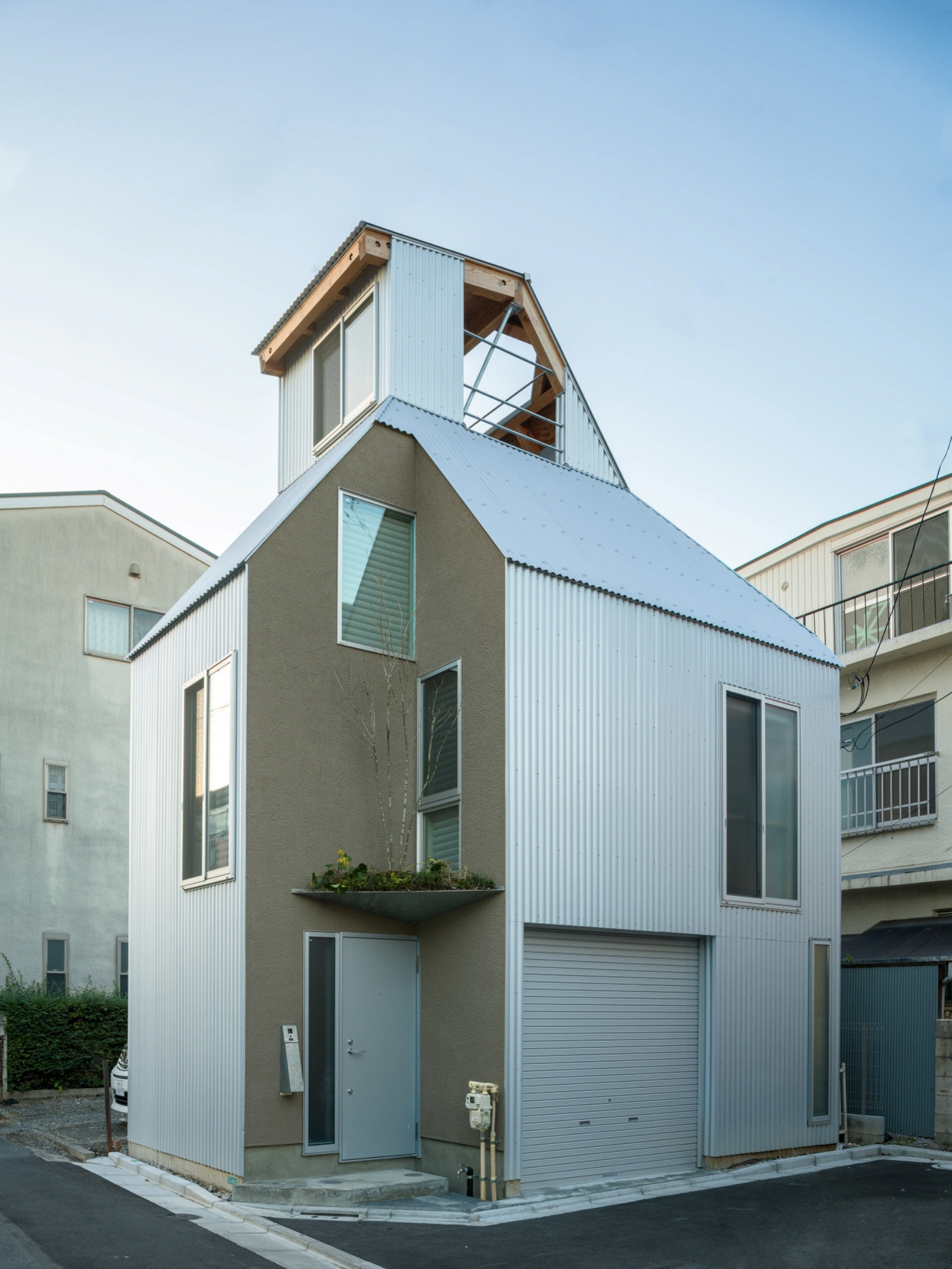 Small House on a Corner Lot by KOMINORU Design — A corrugated metal-clad corner structure on Tokyo's constrained 30-square-meter lot demonstrates how regulatory constraints become formal generators.