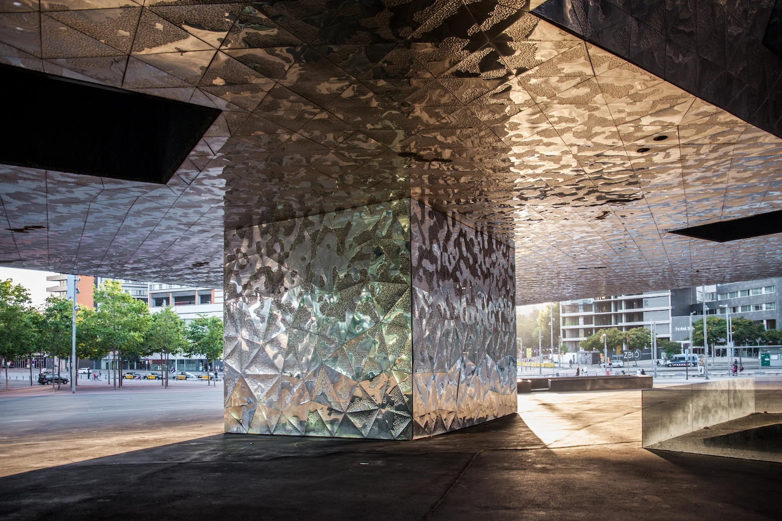 Museu Blau by Herzog & de Meuron — Beneath the massive cantilevered concrete structure, leaf shadows create an intricate linear pattern across the ceiling and supporting column surfaces.